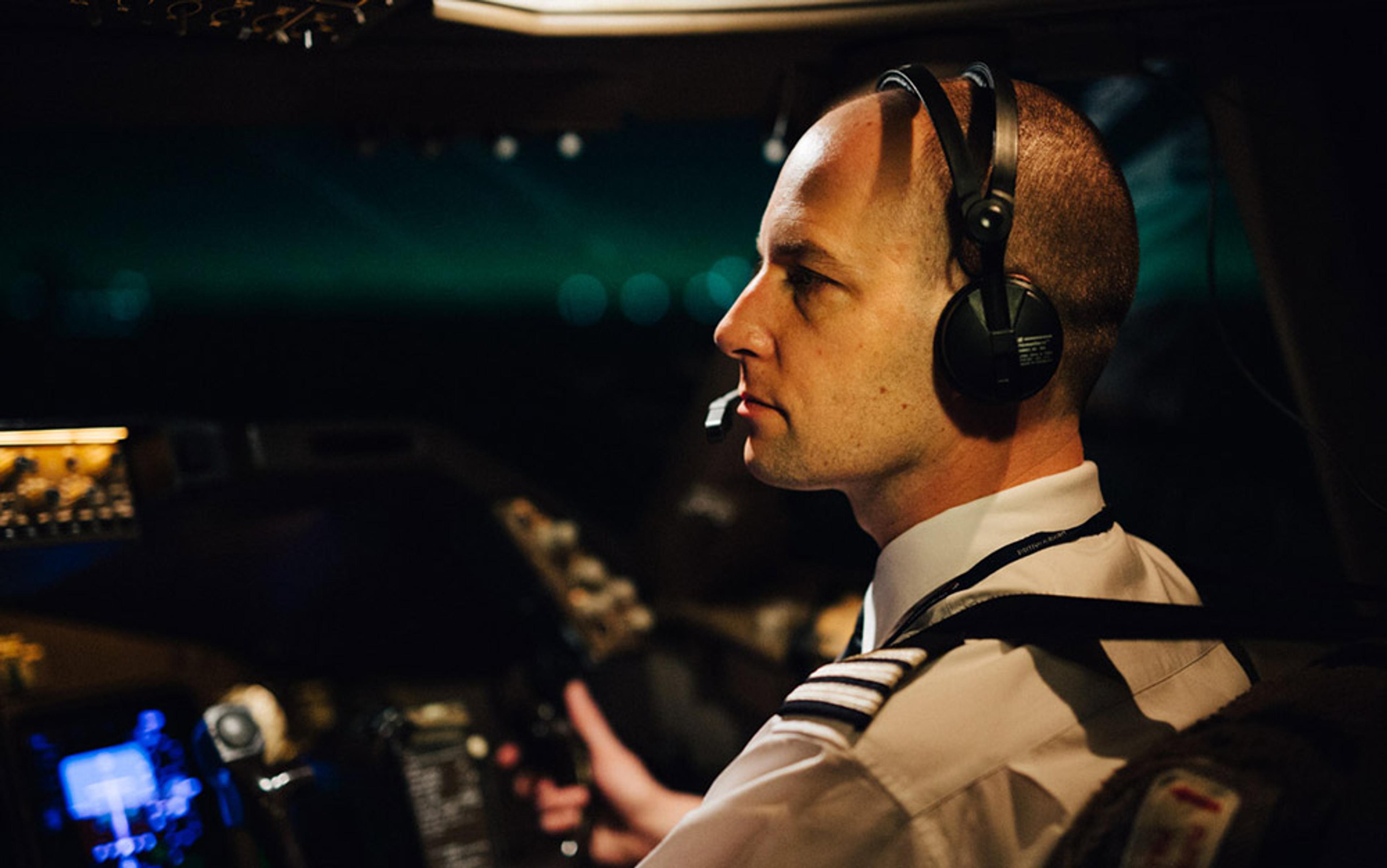 A pilot wearing a uniform and headset in an aeroplane cockpit, concentrating and looking straight ahead.