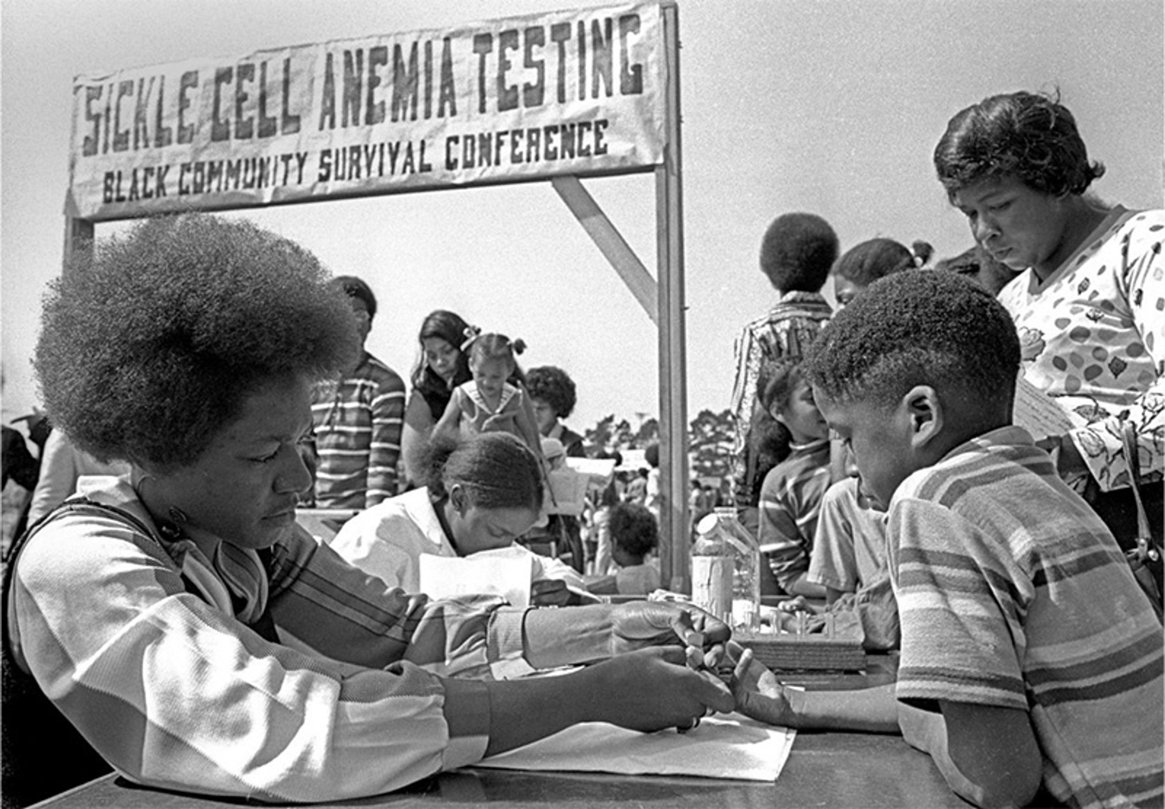 Black-and-white photo of a sickle cell anaemia testing event at a Black Community Survival Conference, with people getting tested outdoors.