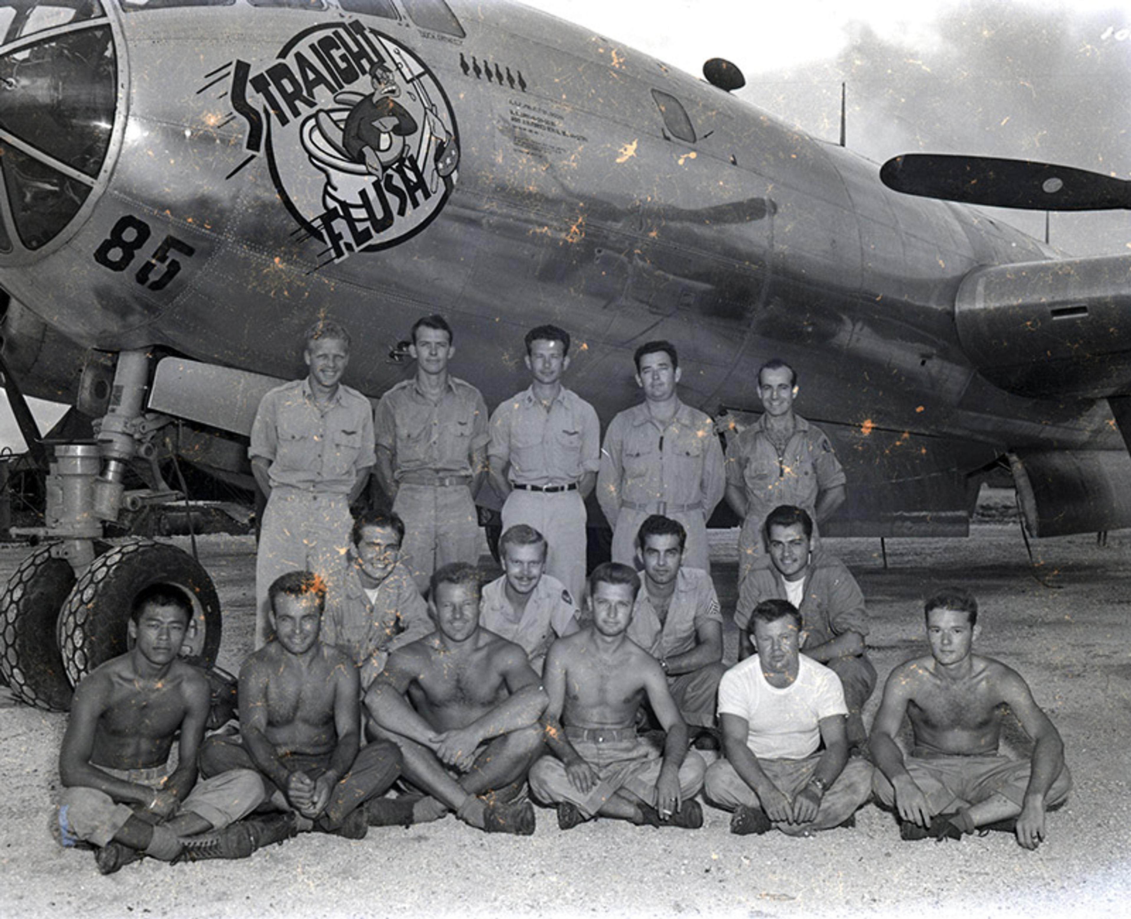Black and white photo of a group of men, some in uniform, some topless, posing in front of a plane with “Straight Flush” nose art and the number 85 visible.