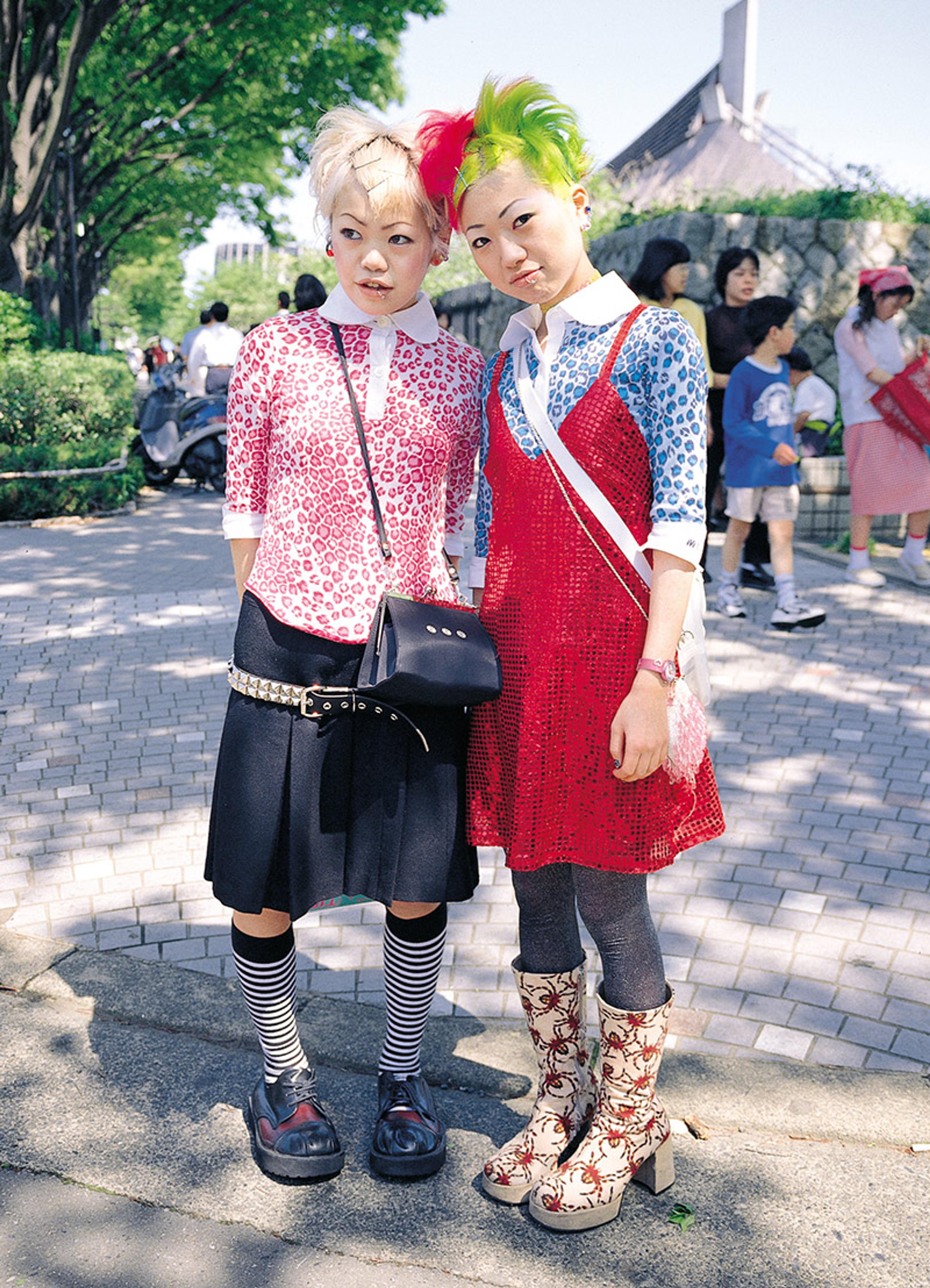 Two Japanese people wearing colourful outfits with bold patterns standing on a paved path outdoors, with others in the background.