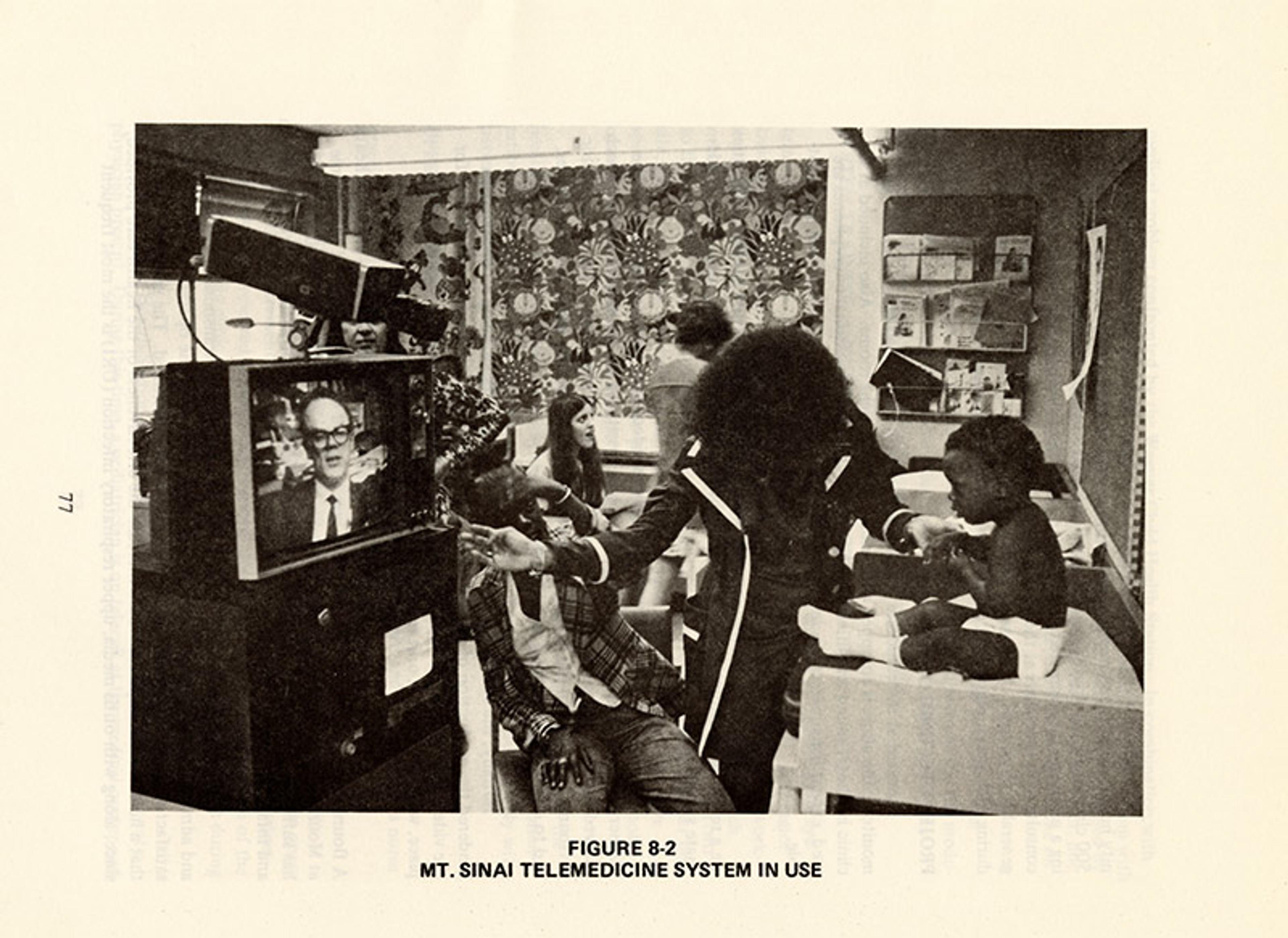 Vintage photo of a telemedicine system in use at Mt. Sinai, with a doctor on a screen and patients in a clinic room.