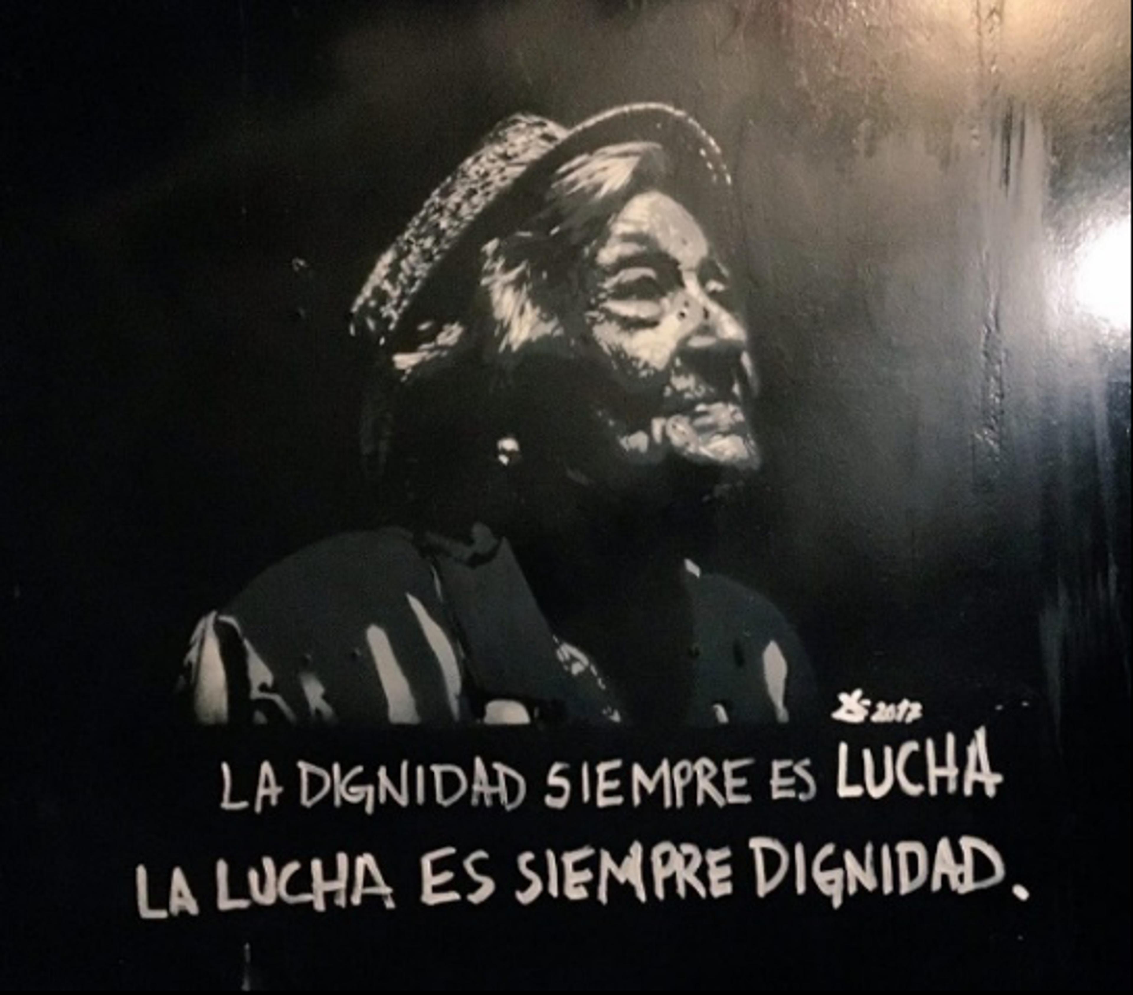 Painting of an elderly woman in a hat with Spanish text, “La dignidad siempre es lucha, la lucha es siempre dignidad” on a dark background.