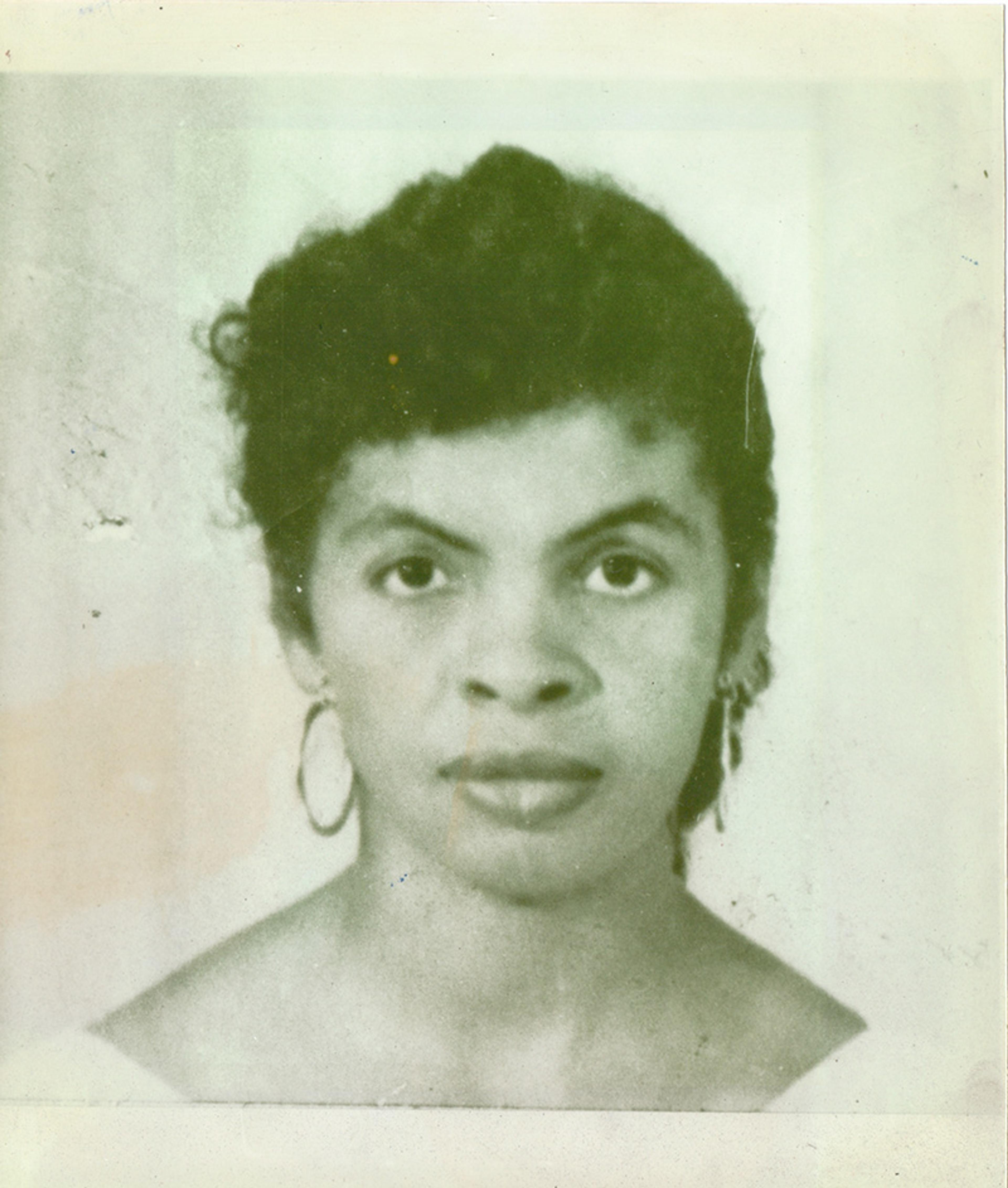 Black-and-white photo of a woman with short curly hair wearing hoop earrings, looking directly at the camera with a neutral expression.
