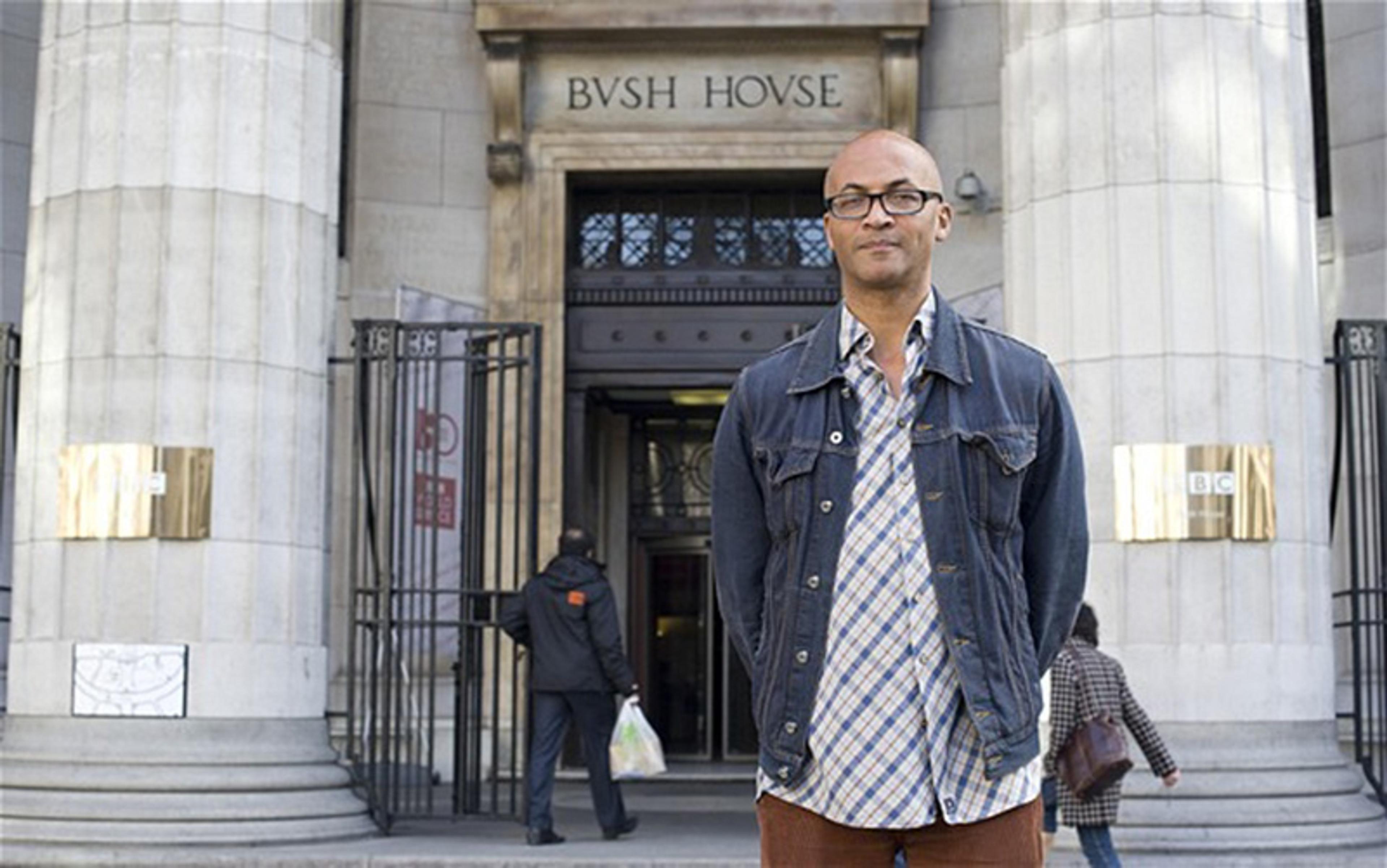 A man standing in front of Bush House in London wearing a denim jacket and plaid shirt with people entering the building.