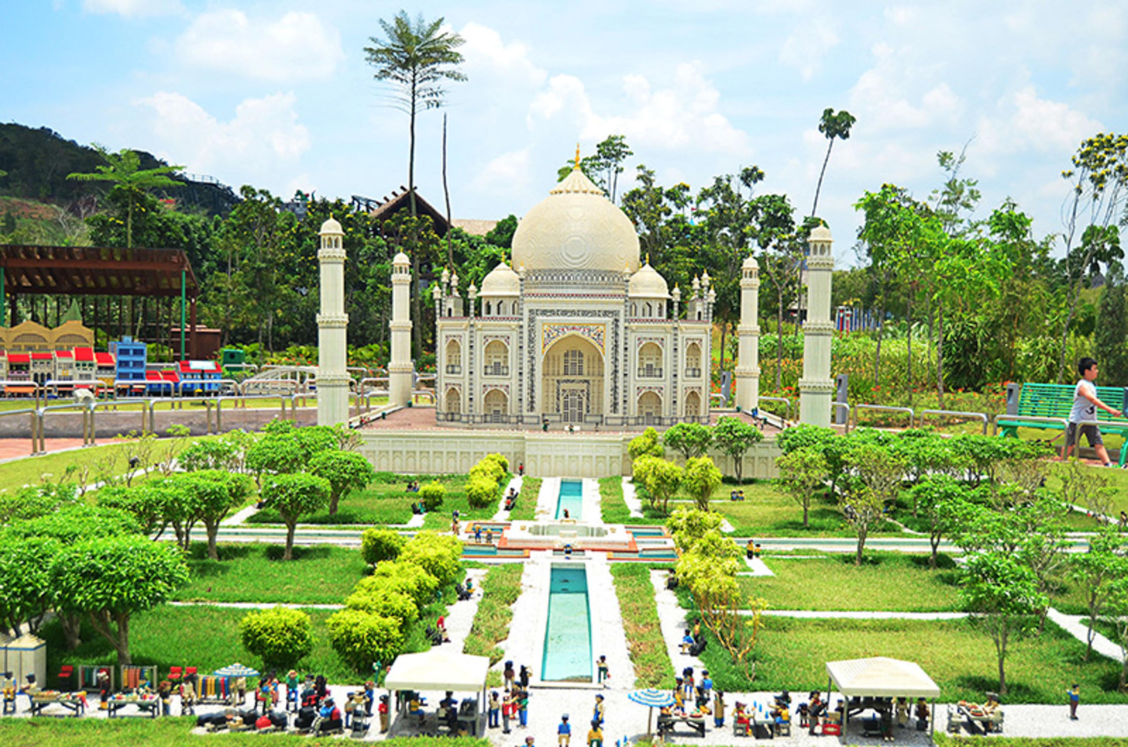 A detailed Lego Taj Mahal model with surrounding garden, people and trees, set in an outdoor theme park on a sunny day.