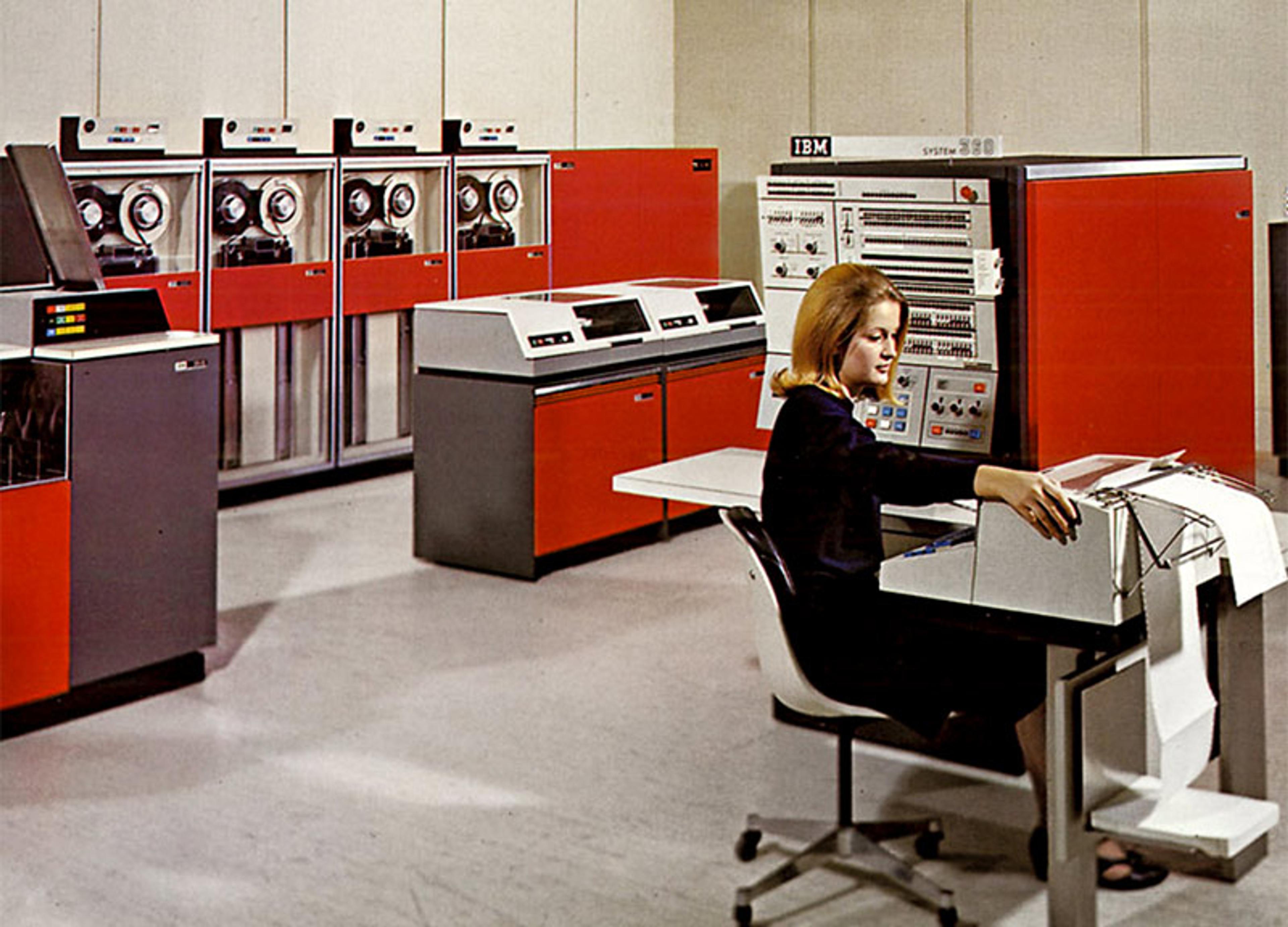 A woman working with an IBM System/360 mainframe in a 1960s computer room with tape drives and large consoles.