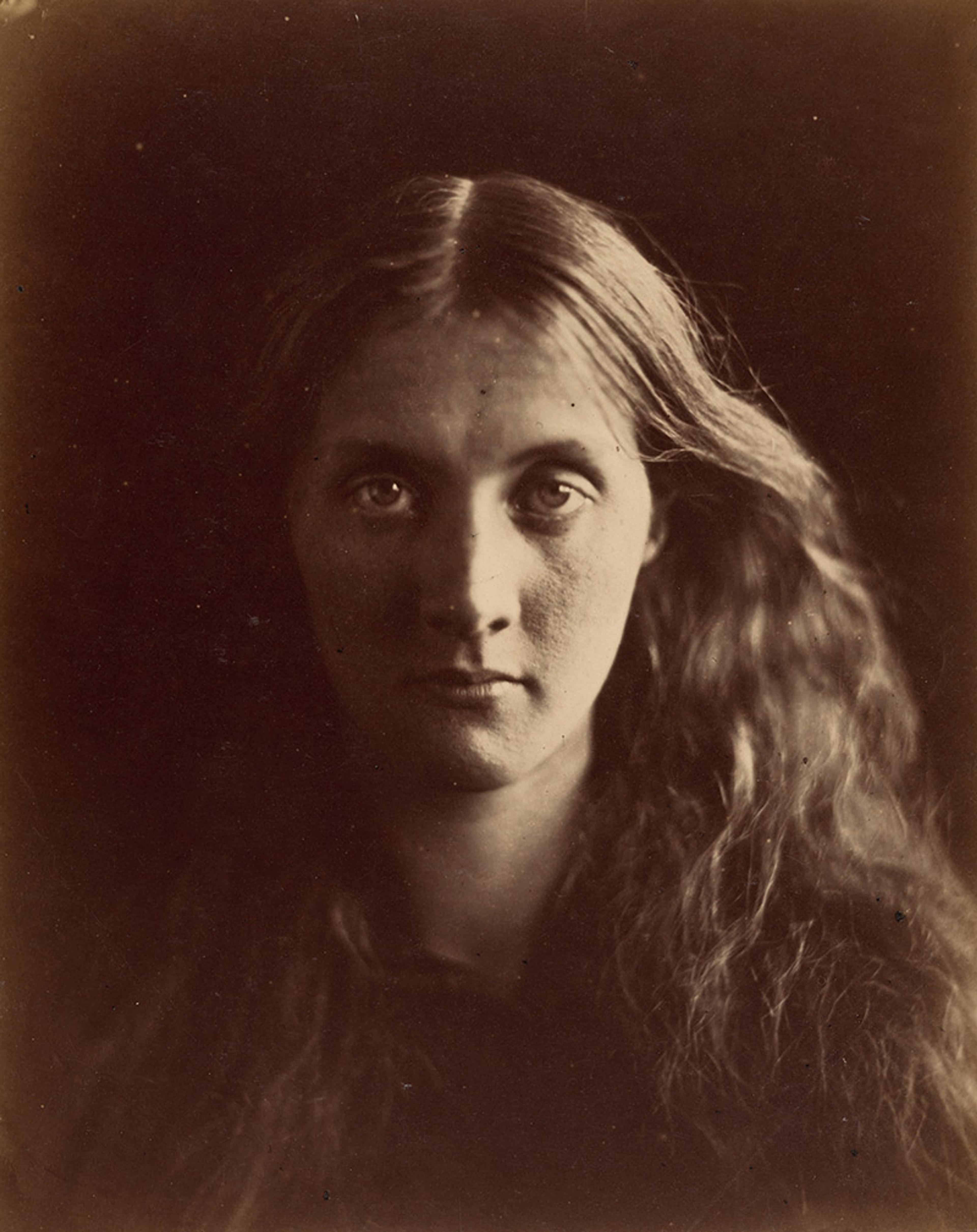 Sepia-toned photograph of a young woman with long wavy hair, facing forward with a neutral expression against a dark background.