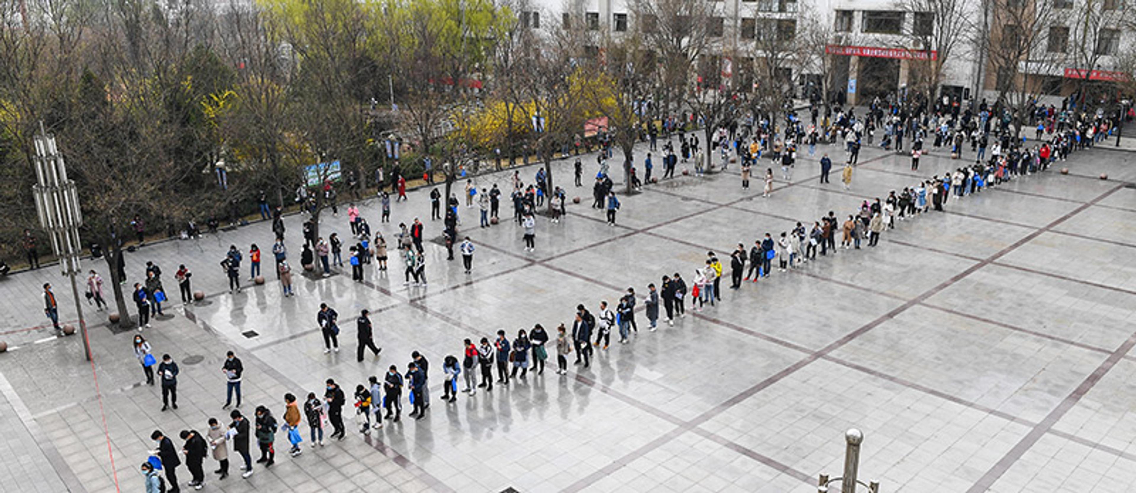 Many young Chinese people are pictured in a long line outside an examination centre in a commercial district