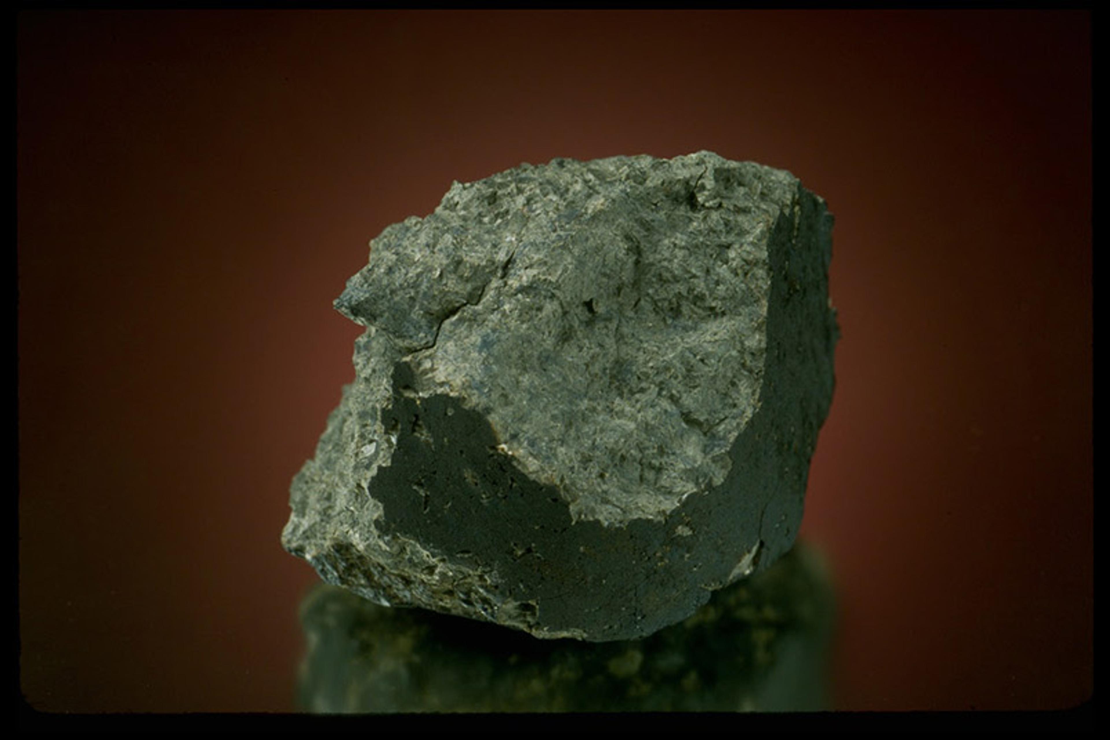 A piece of greenish rock set on a dark mirrored surface