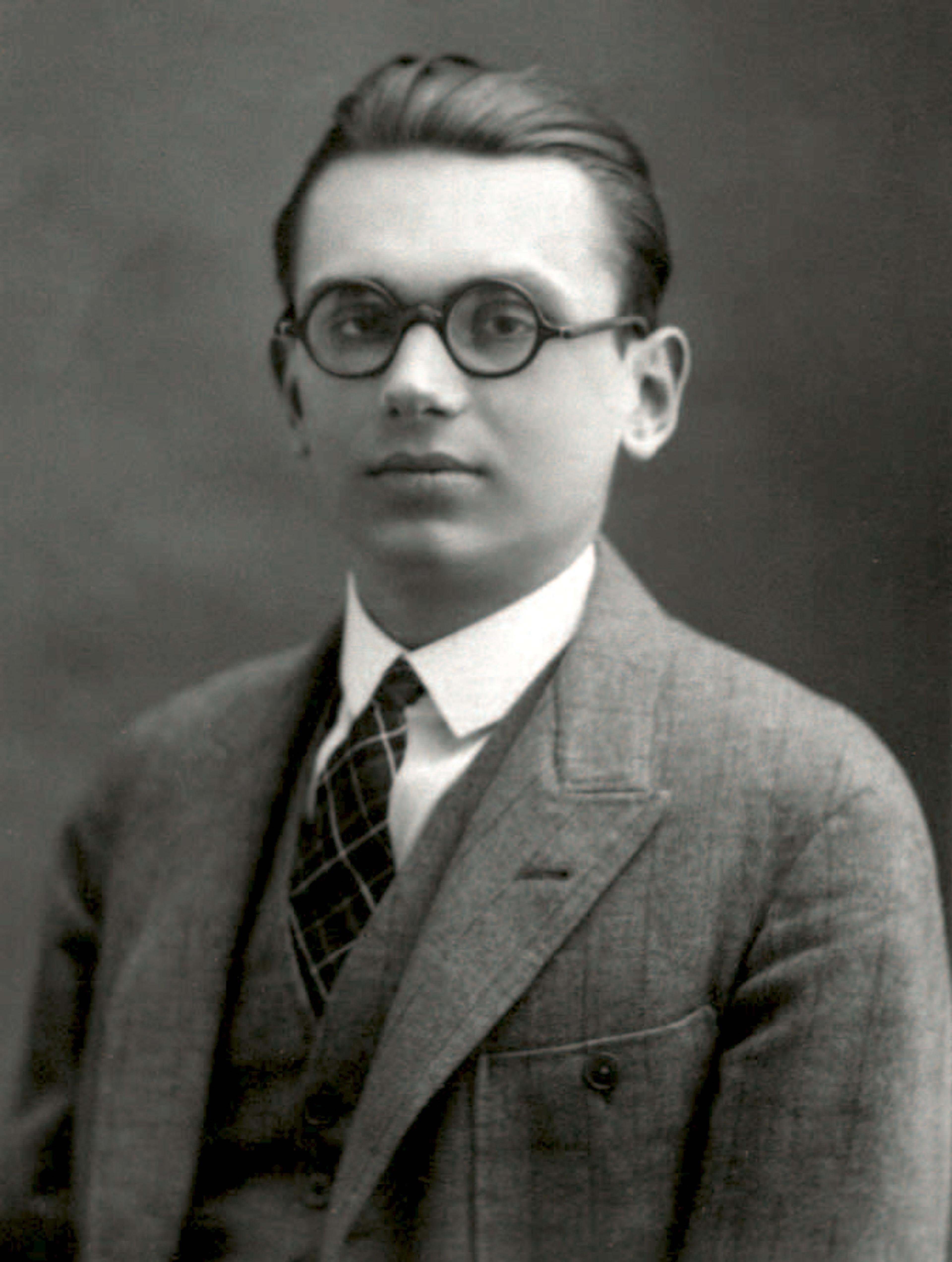 Vintage photo of a man with glasses in a suit, tie and vest, posed in front of a plain background.