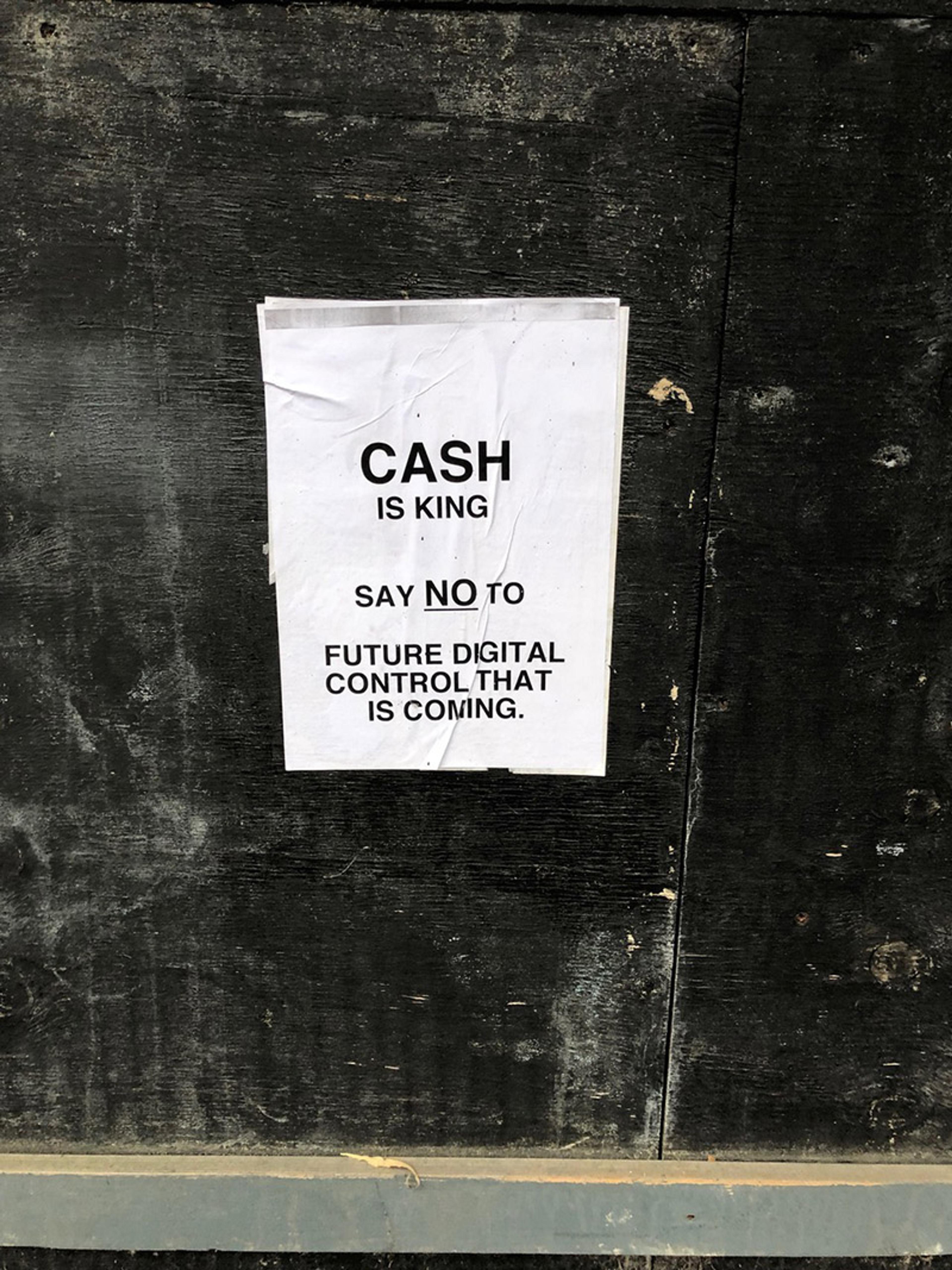 A handmade poster stuck to a black wall reads cash is king say no to future digital control that is coming