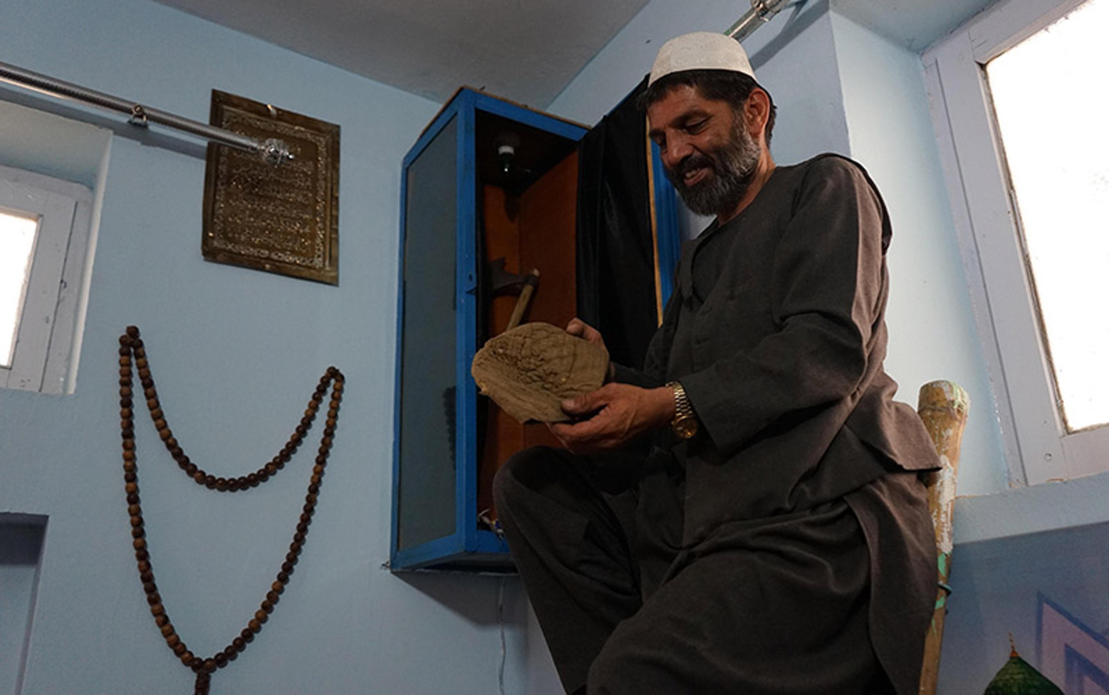 A smiling man displays an old cap taken from a wall cabinet