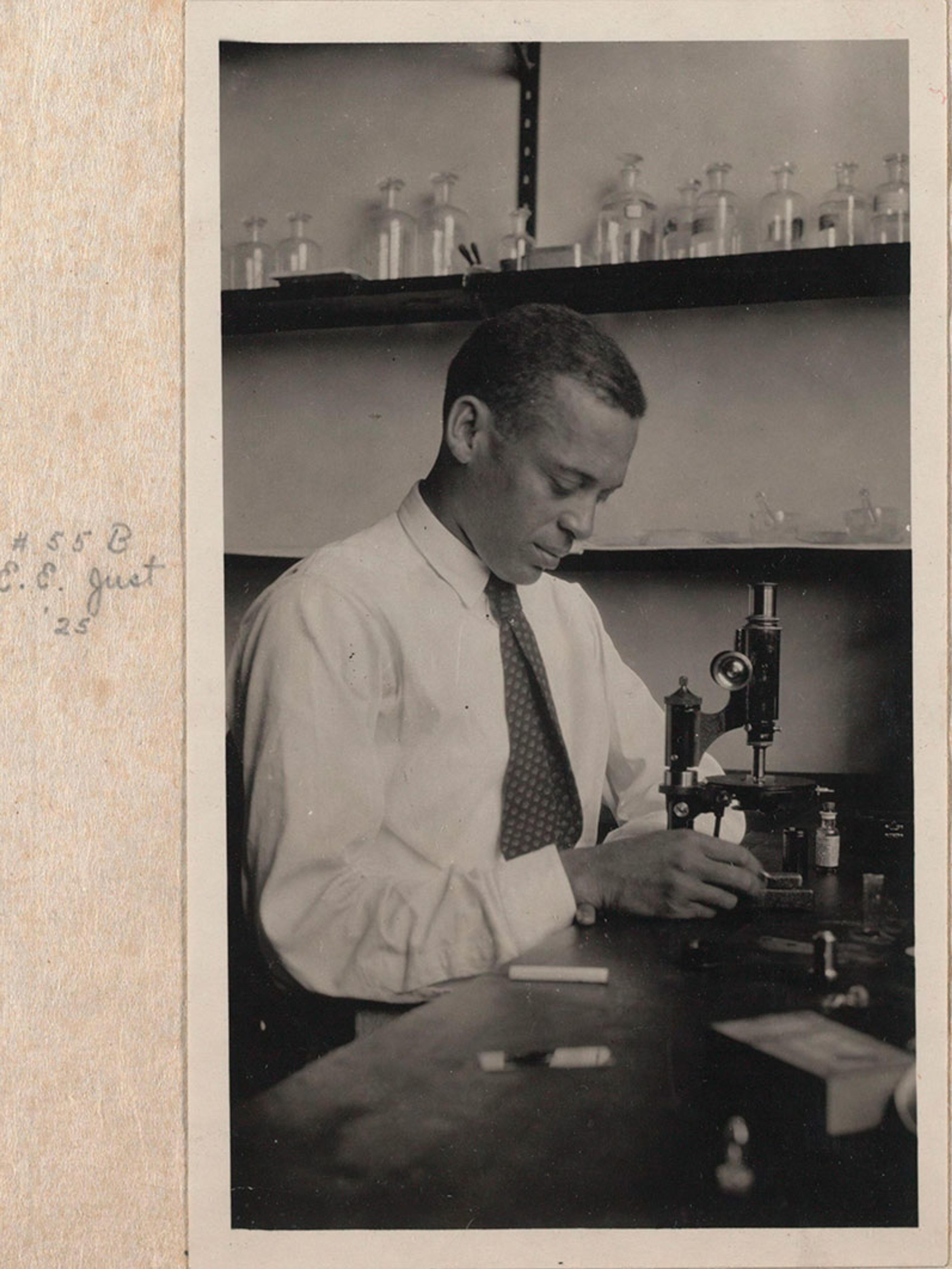 An African American scientist at work in a lab with a microscope. The image is an older print within a photo album