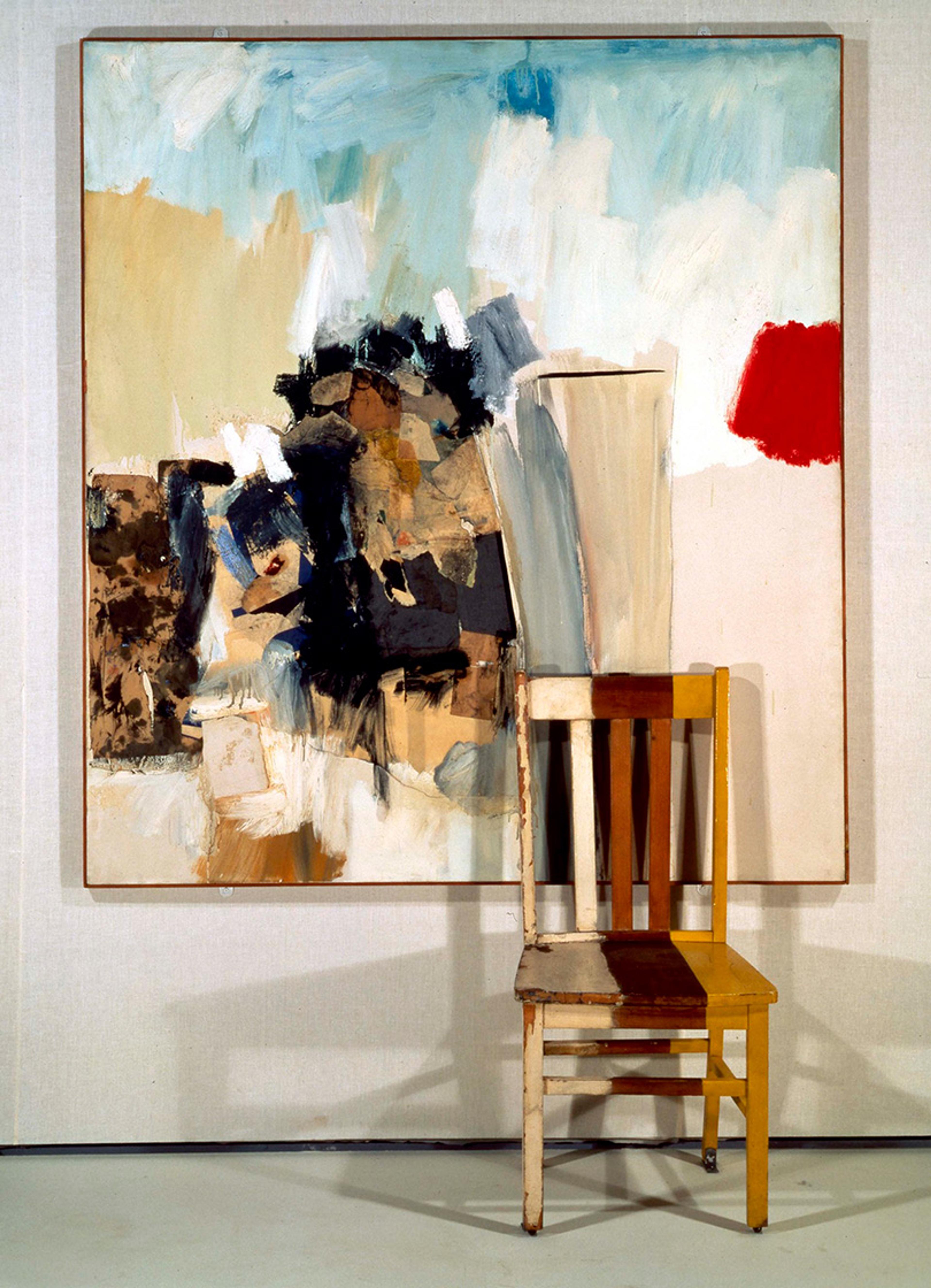 An abstract painting with blue, white, black, and beige colours is displayed on a wall. A worn, multicoloured wooden chair is placed in front of the painting. The painting and chair overlap, creating a visually interesting contrast between the 2D art and the 3D object.