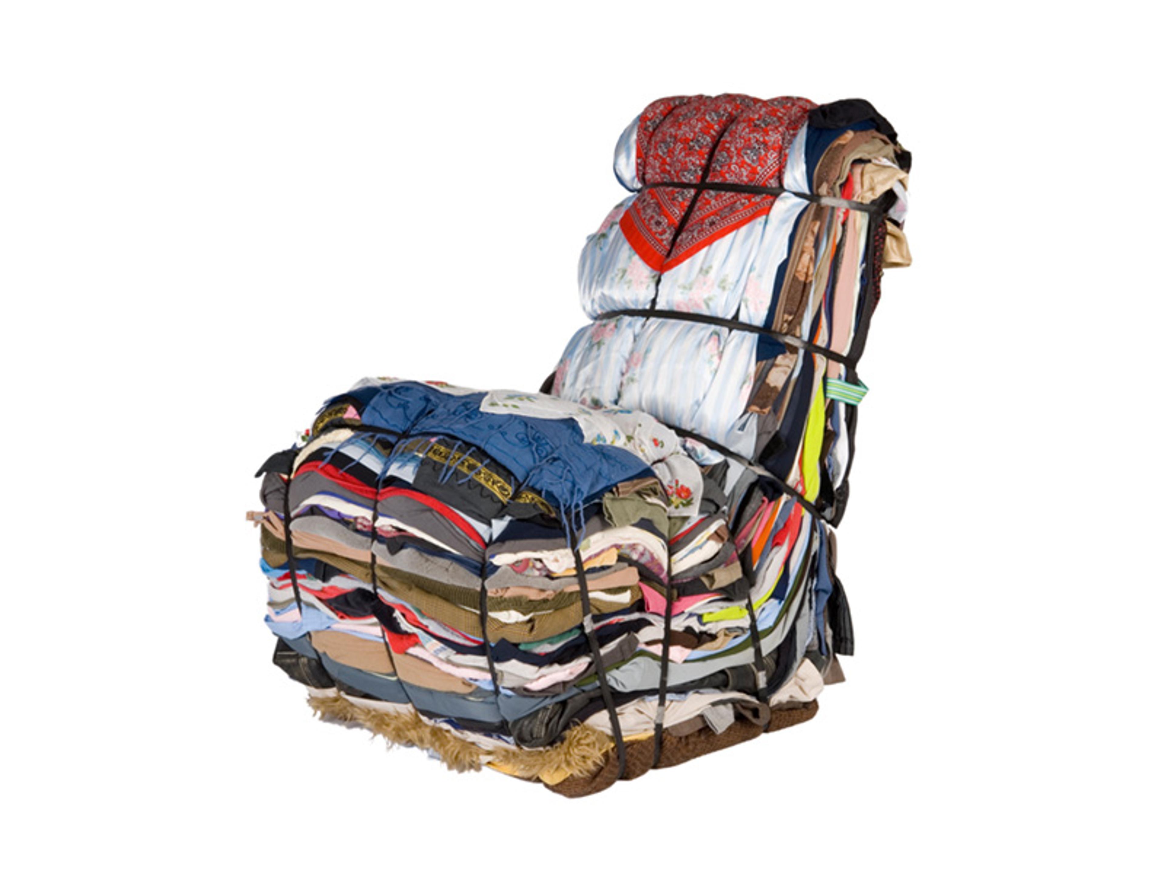 A chair made up of colourful, assorted clothes tightly bound together with black straps, creating a visually interesting and unique piece of furniture on a white background.