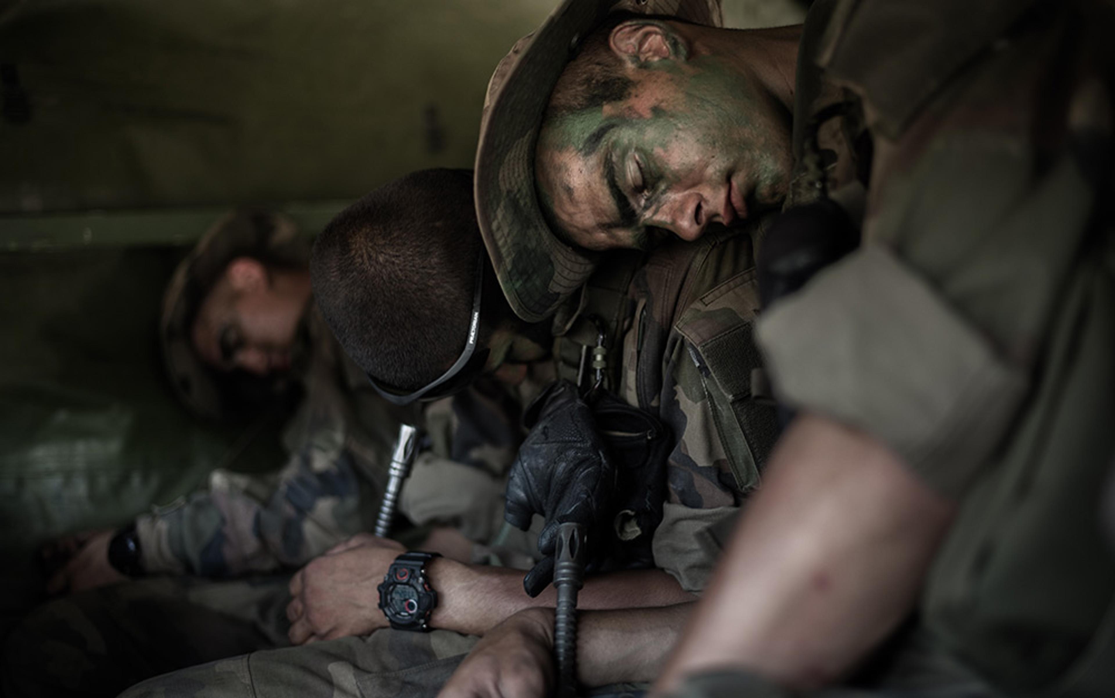 Three soldiers with camouflage face paint and uniforms asleep inside a military vehicle.