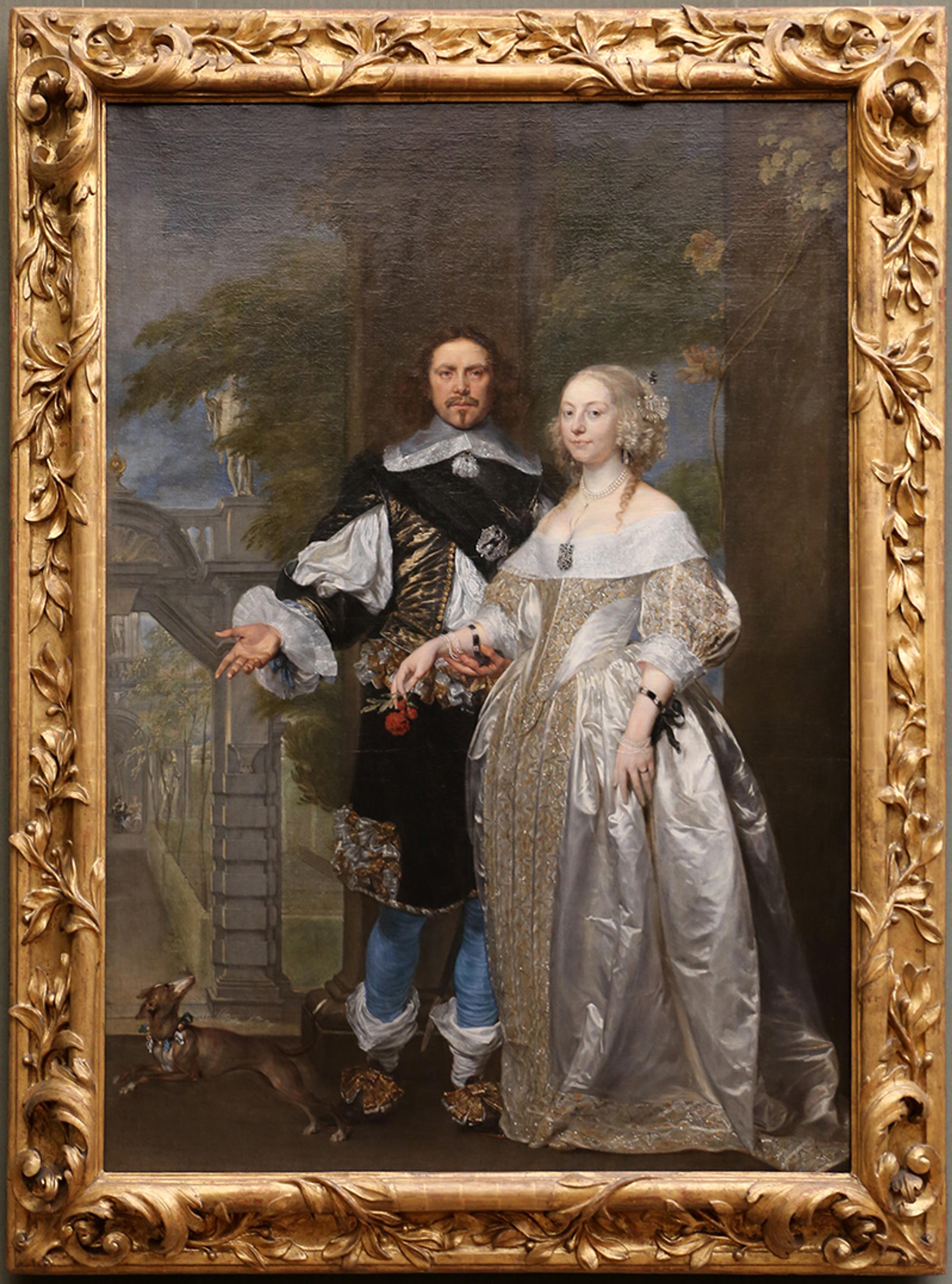 A framed painting of a historical couple in elaborate attire stands together. The man, on the left, holds a hat and wears a black and gold outfit, while the woman, on the right, wears a silver gown with intricate details. A small dog lies at their feet. Trees and architectural elements are visible in the background.
