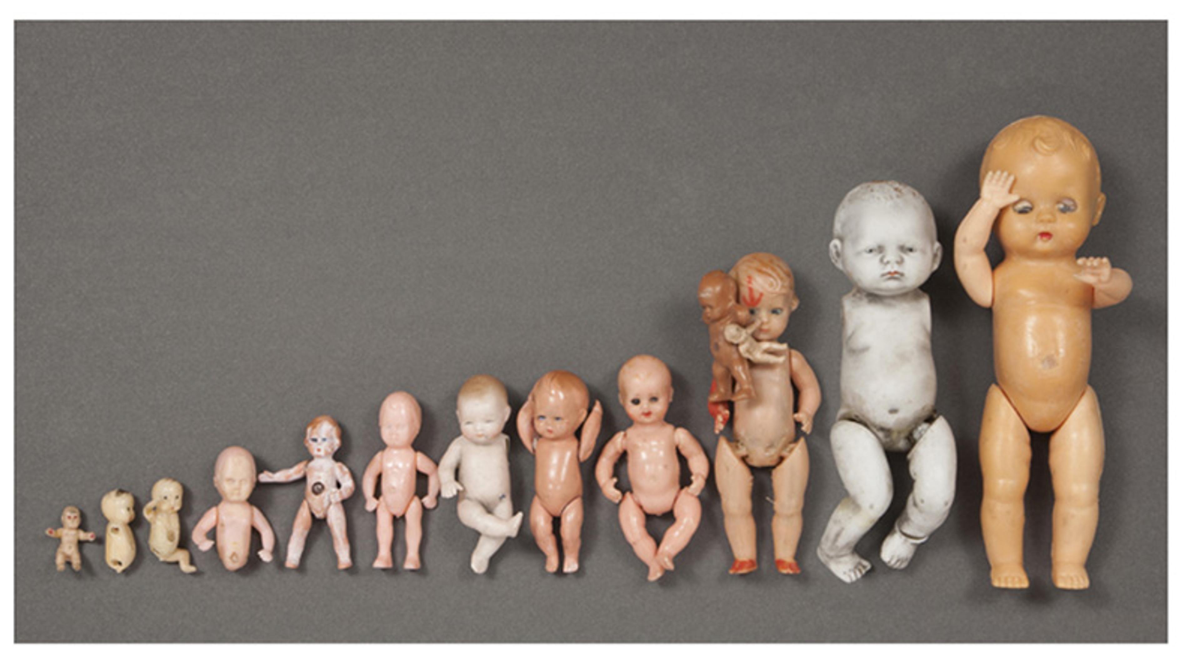 A row of vintage dolls of varying sizes, lined up from smallest to largest, with a grey background.