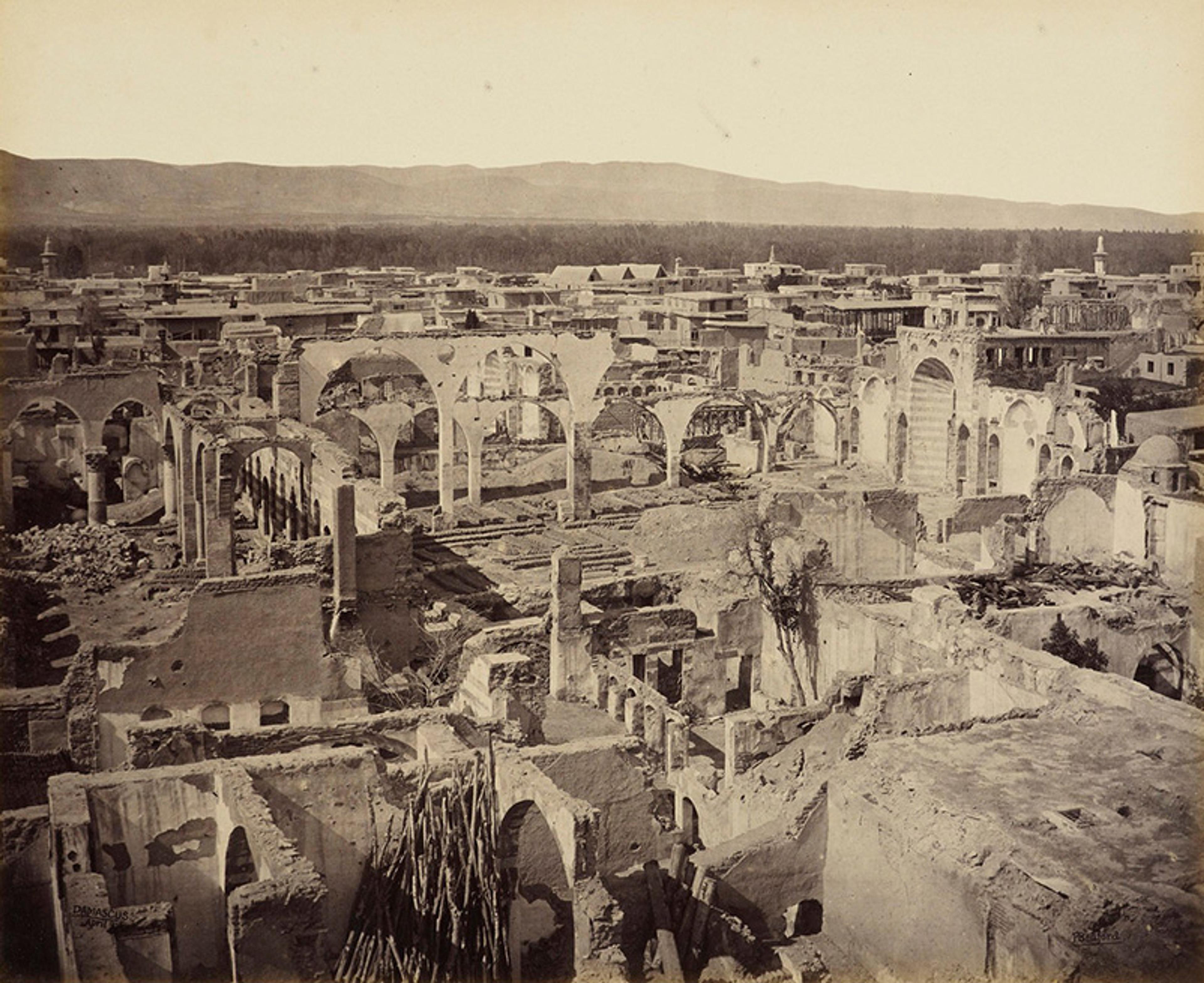 Sepia vintage photograph of the ruins of an ancient city with numerous arches and buildings, extending to the horizon with mountains in the background.