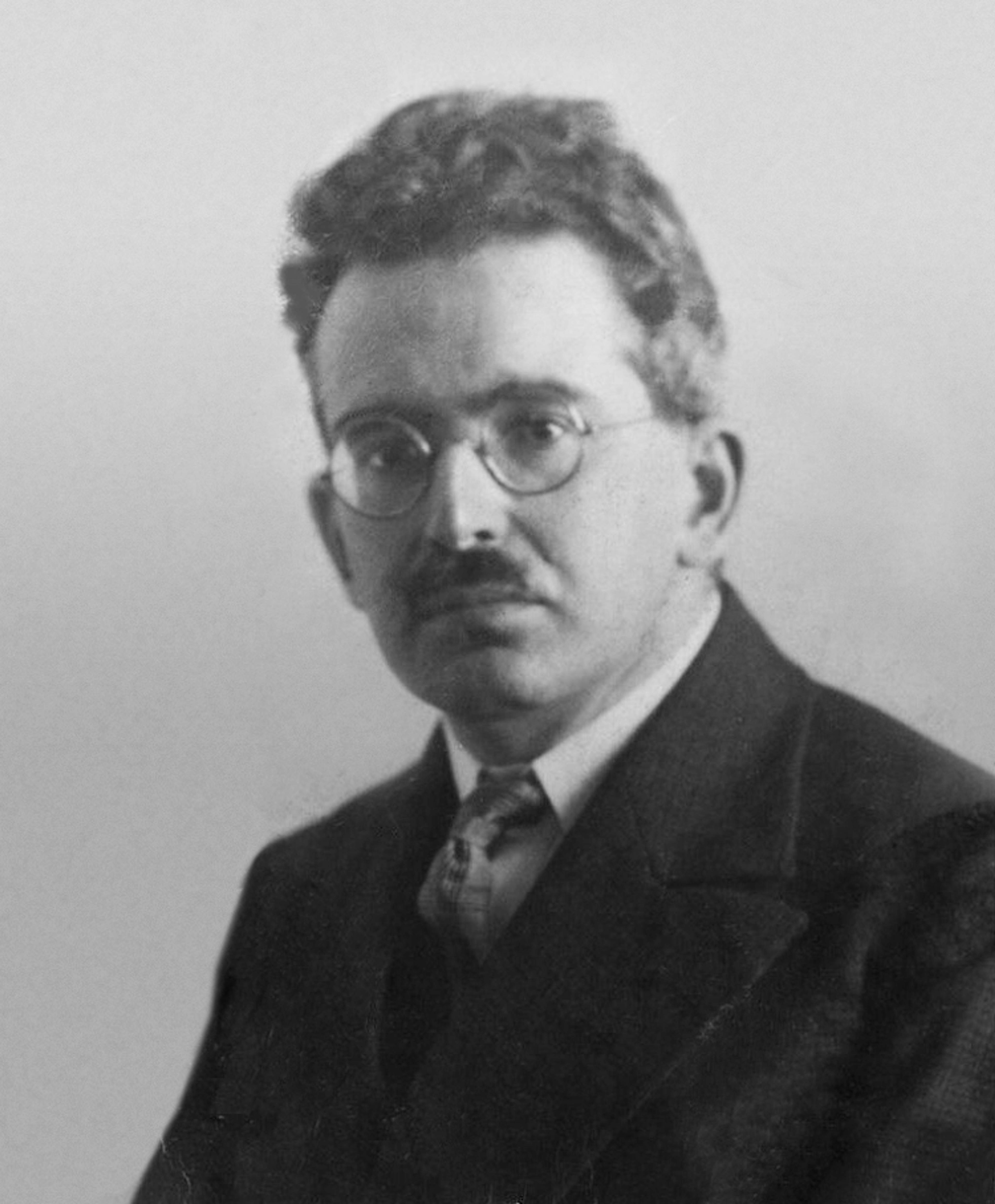 Black and white photograph of a Walter Benjamin, wearing glasses, a suit and tie, looking at the camera.