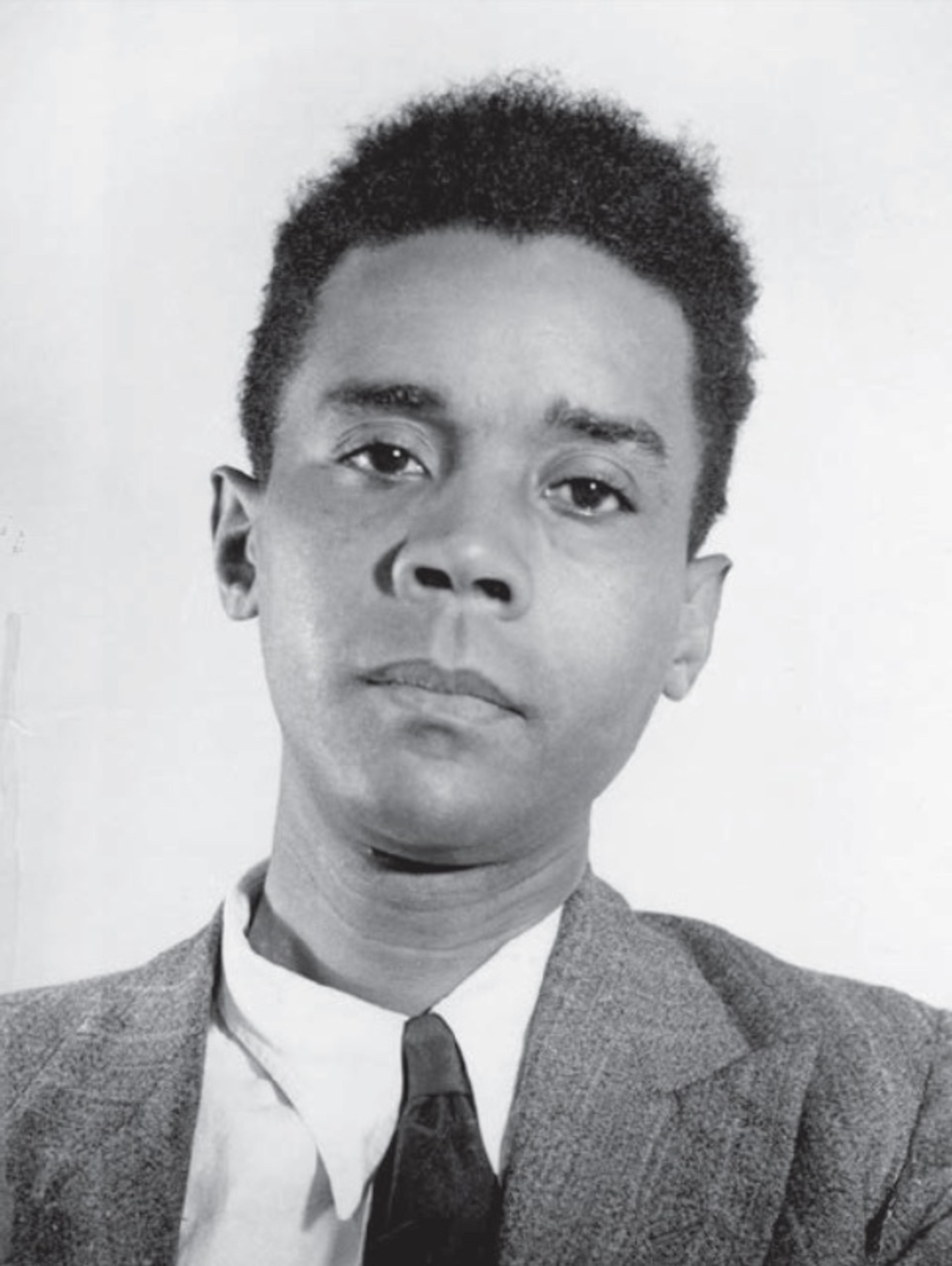 Black-and-white portrait photo of a Black man in a suit and tie against a plain background, looking directly at the camera.