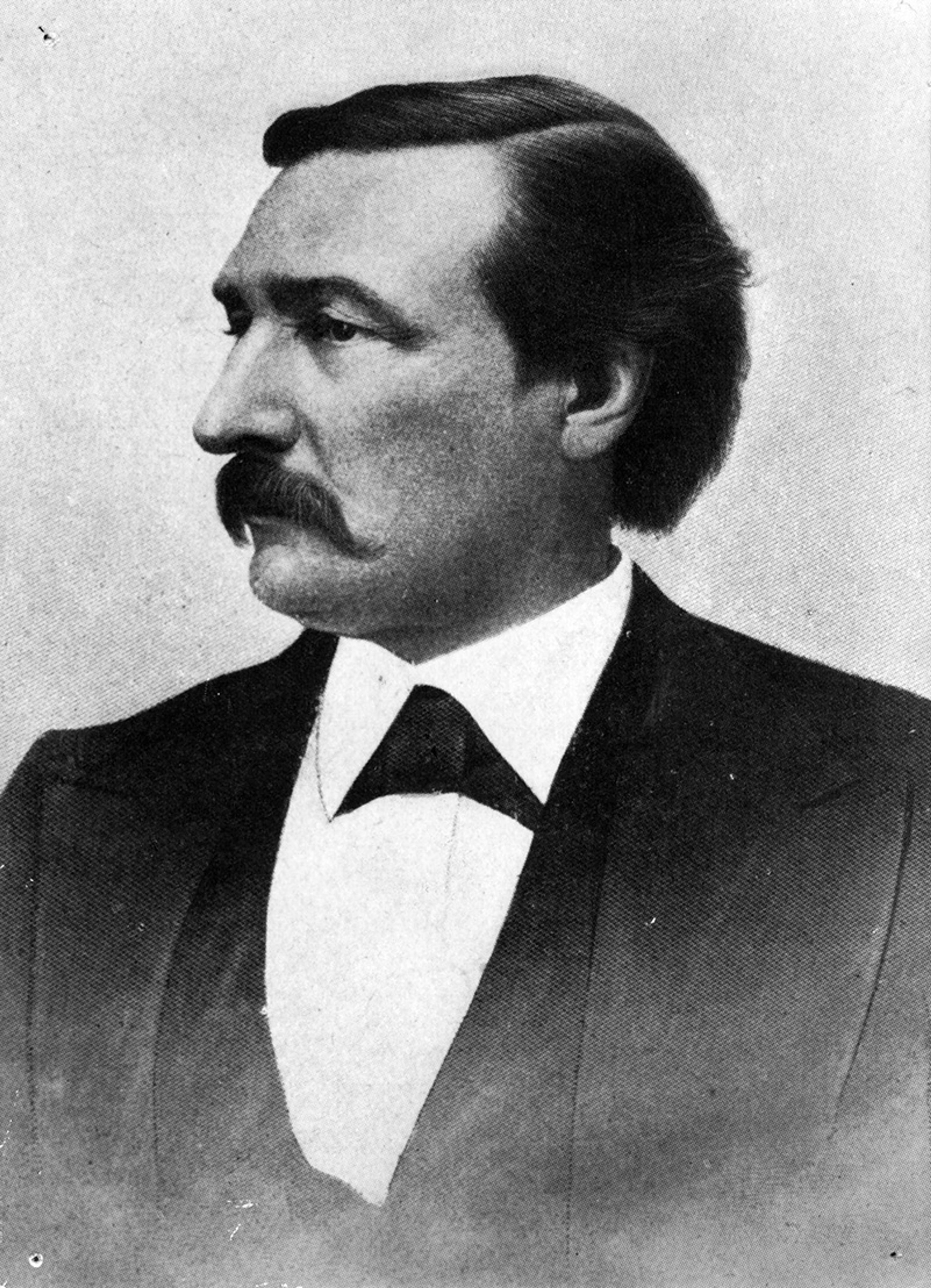 Black-and-white photo of a man with a moustache wearing a suit and tie, facing left, with a neutral expression.