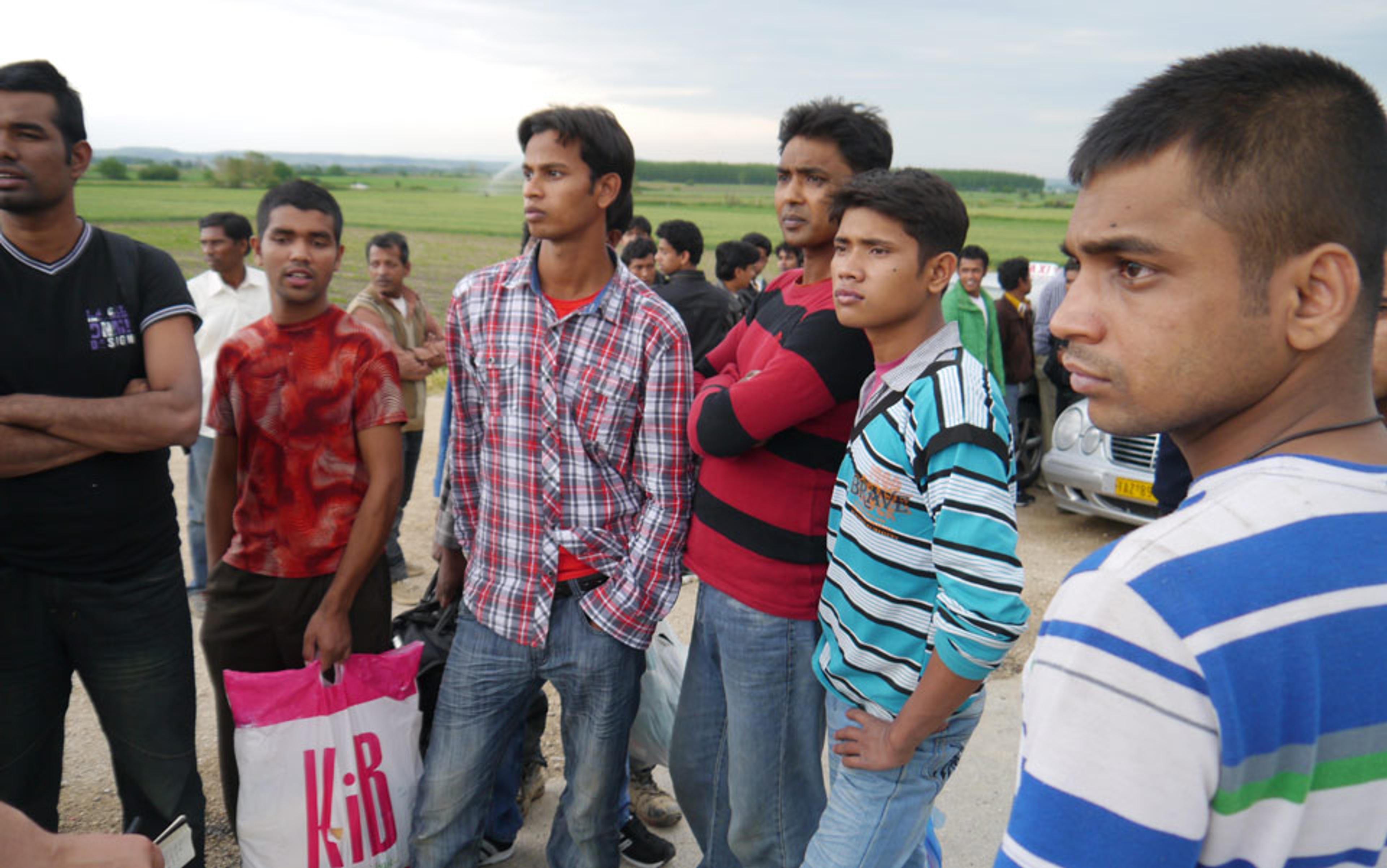 Photo of a group of young men standing outdoors in casual clothing with fields and a cloudy sky in the background.