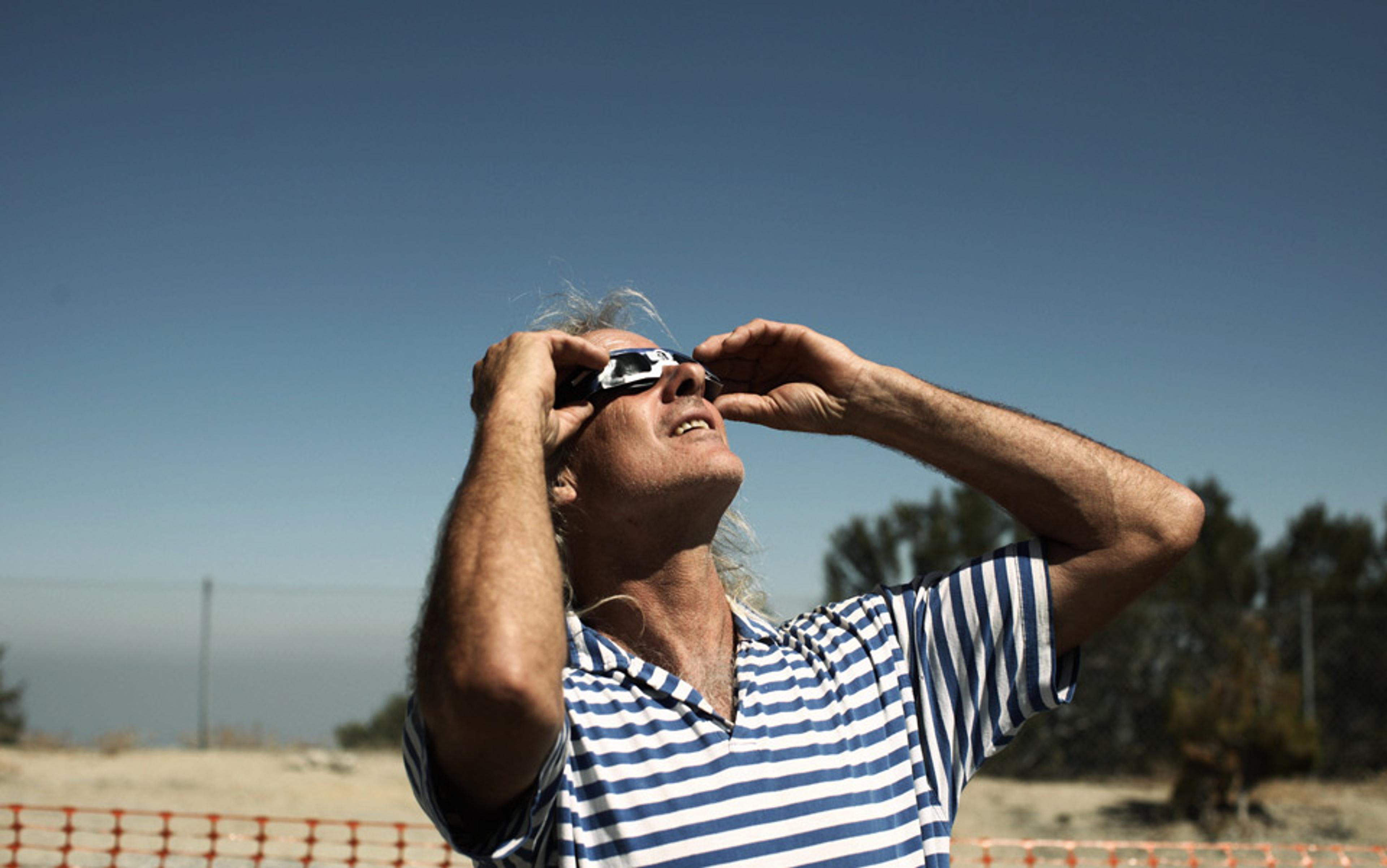 Photo of a person in a blue and white striped shirt looking up, wearing sunglasses, with a clear sky and trees in the background.