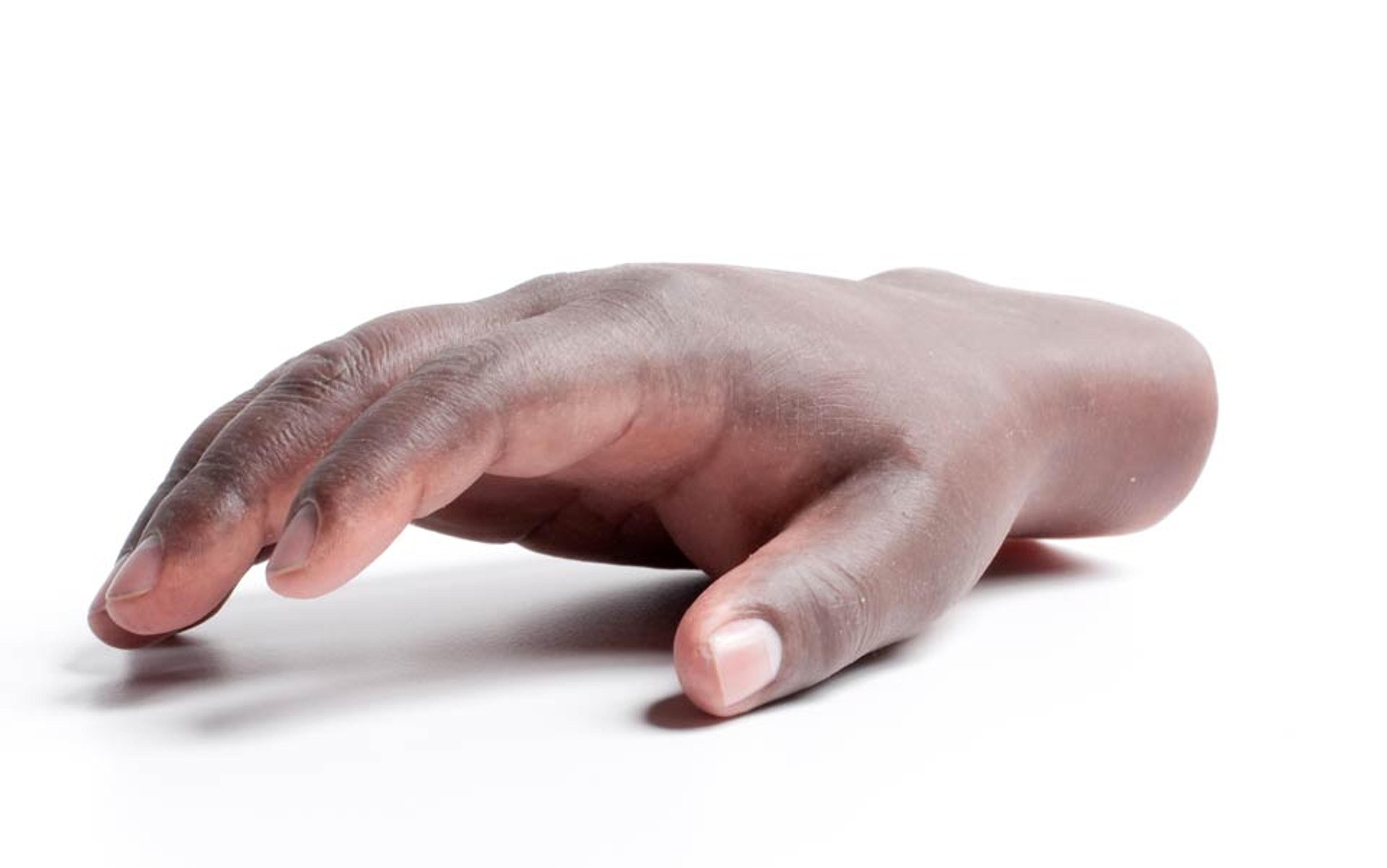 A realistic prosthetic hand with brown skin tone resting on a white surface, positioned in a slightly curved manner.