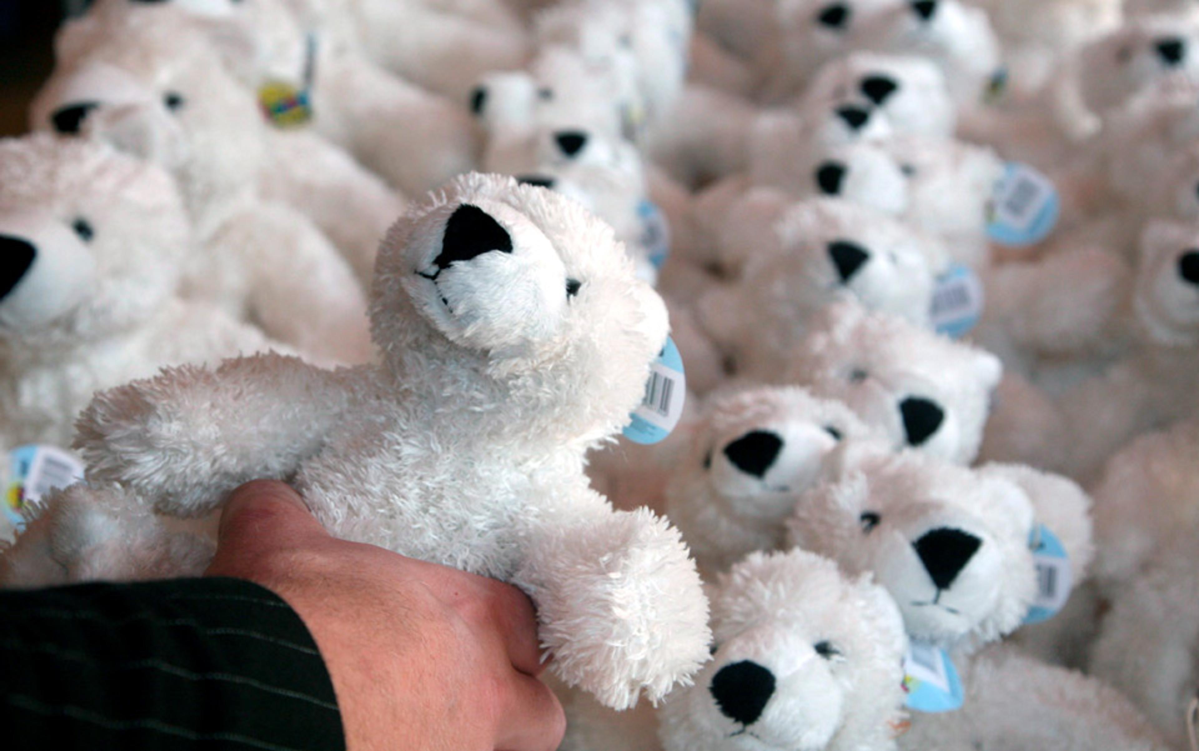 Photo of a hand holding a fluffy white bear toy among a large group of similar bear toys in the background.