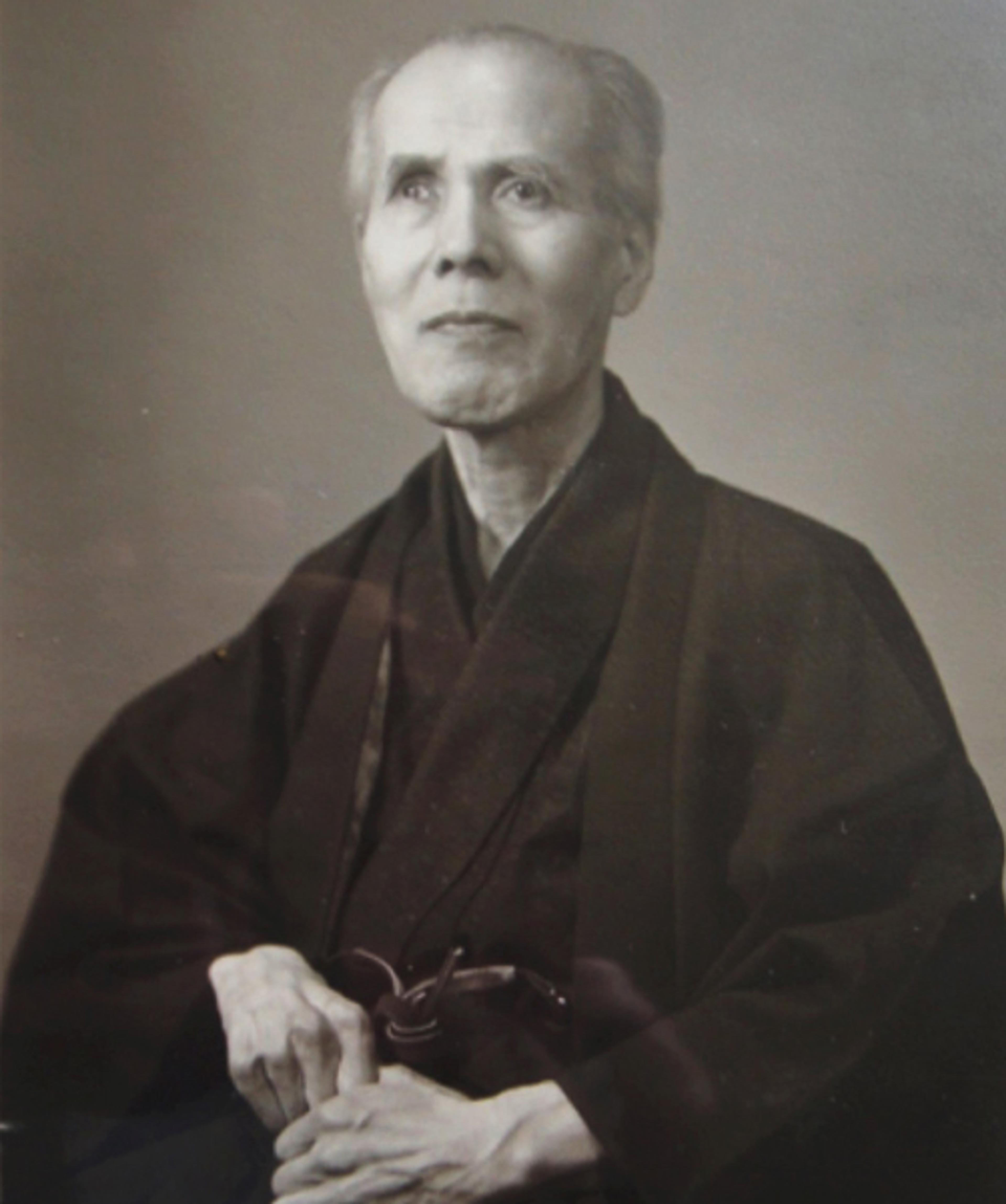 Black and white photo of an elderly person in traditional Japanese attire, looking slightly upwards with a calm expression.