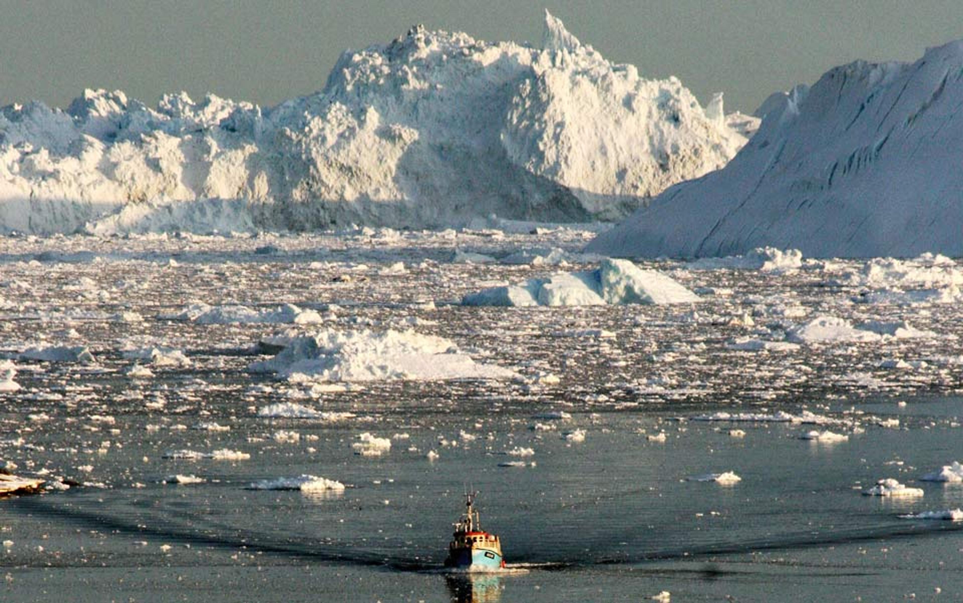 A boat navigating through icy waters with large snow-capped mountains and icebergs in the background.