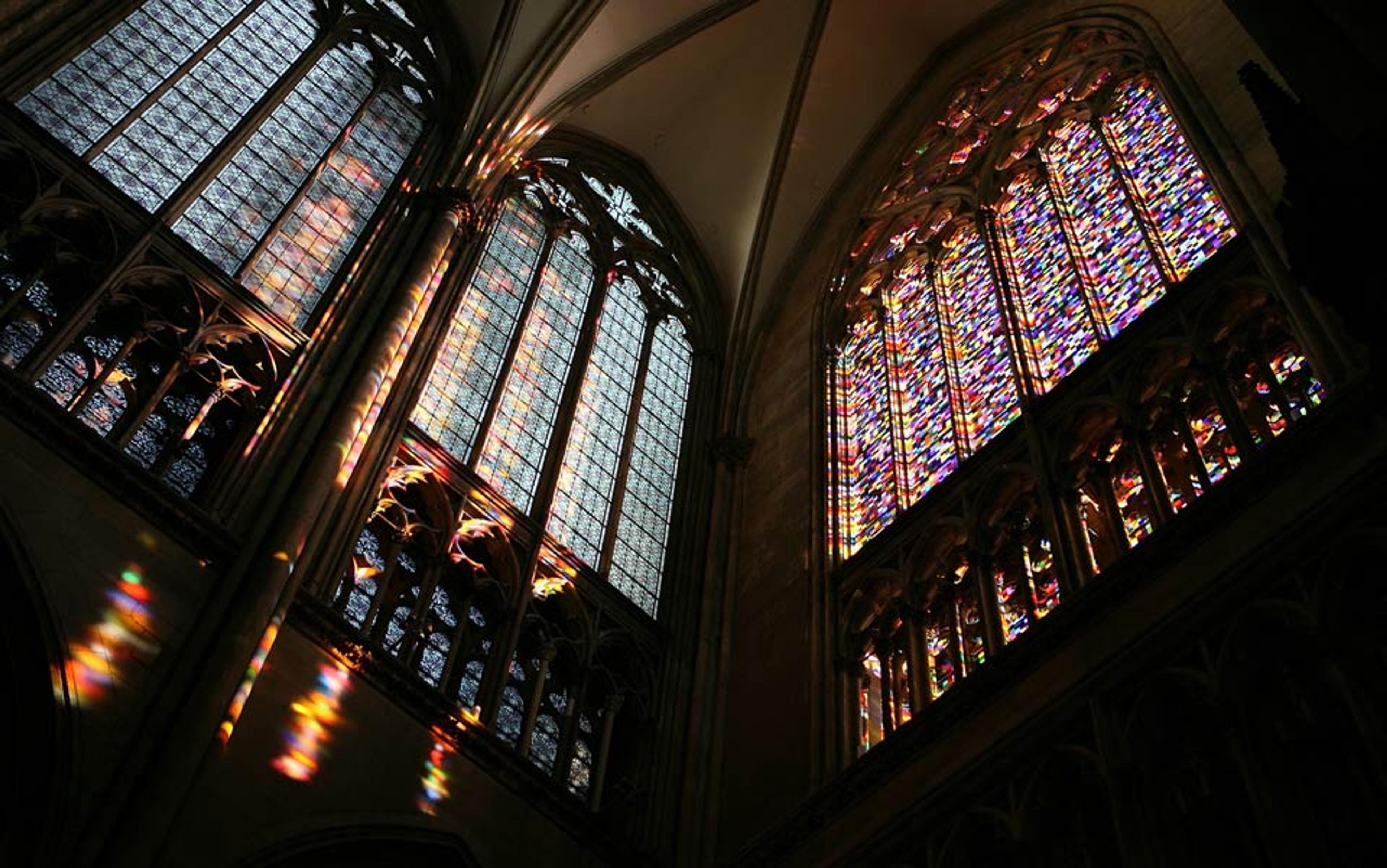 Photo of cathedral interior, stained glass windows casting colourful light patterns on stone walls, Gothic arches in view.