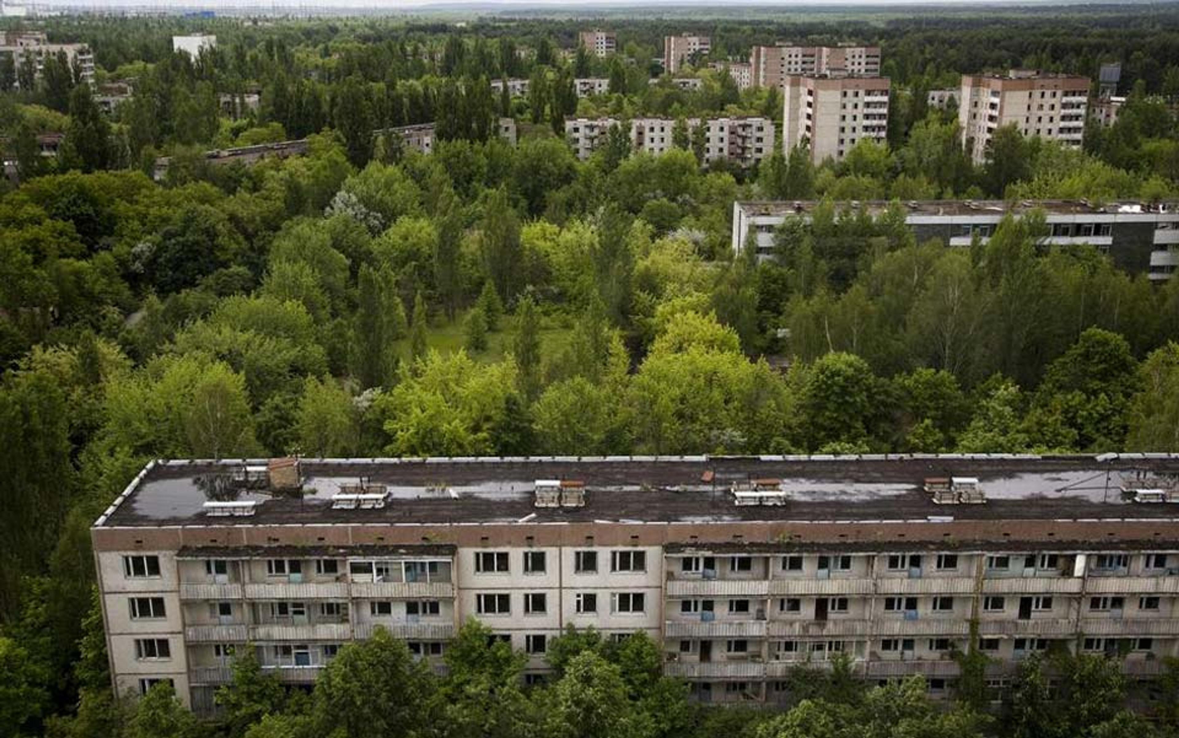 An abandoned apartment building in a green forested area with multiple other deserted buildings in the background.