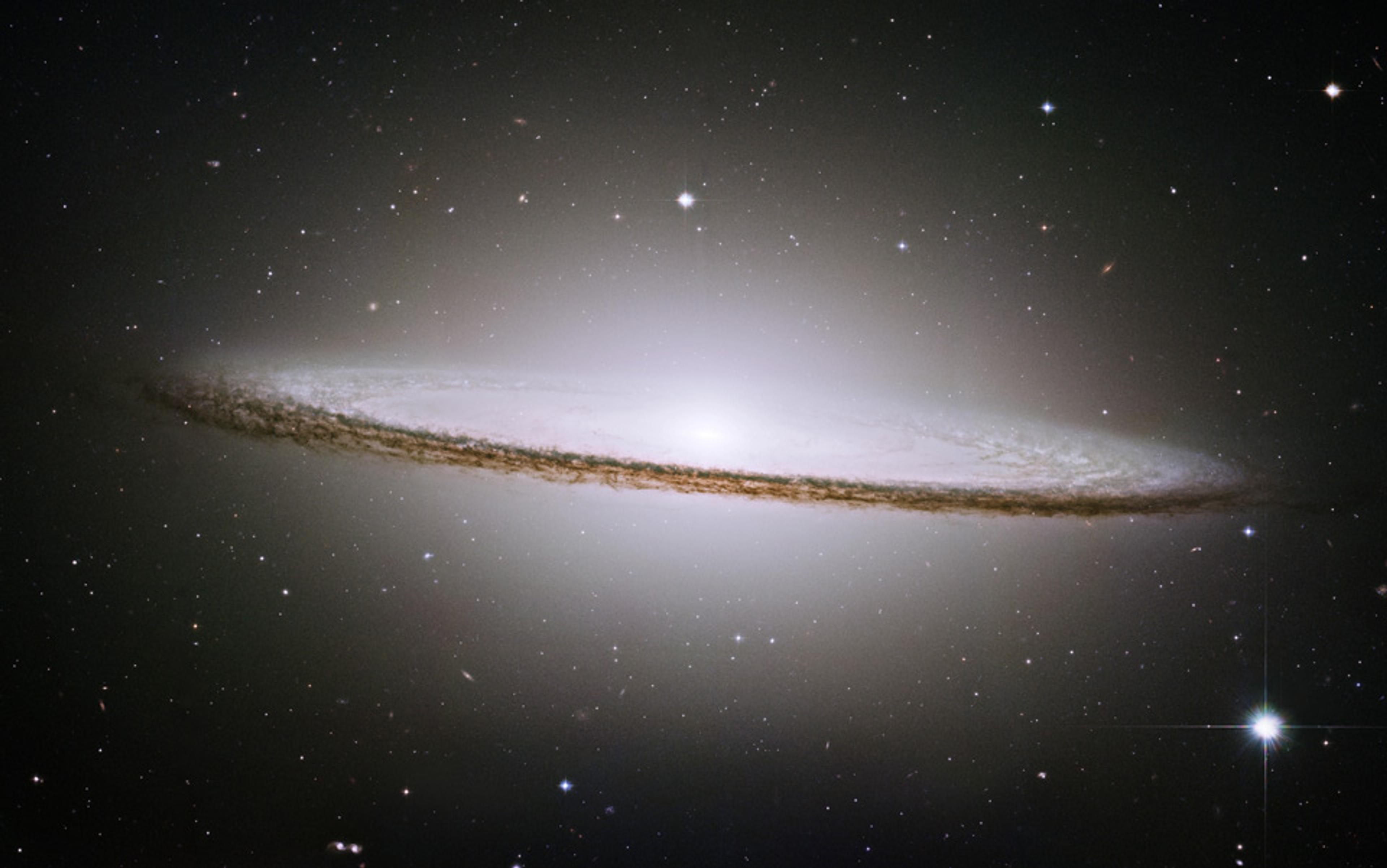 Photo of a galaxy with a bright core and a thin, dark ring of dust. Stars are scattered in the background of space.