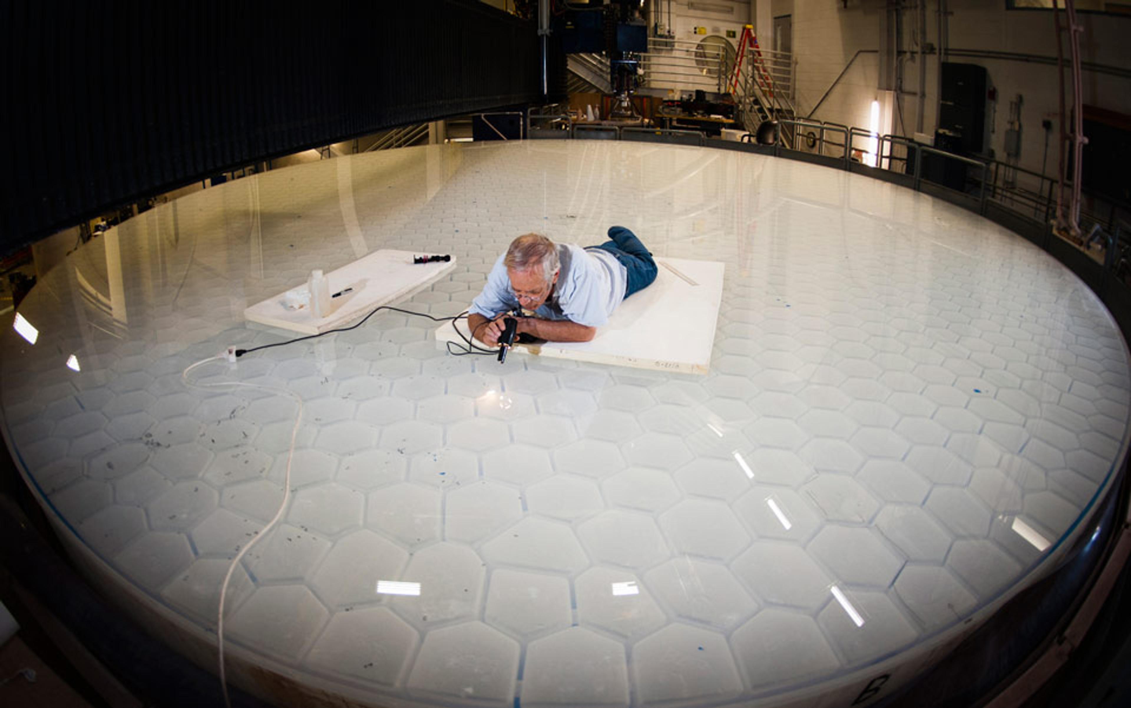 Photo of a man lying on a large hexagonal-patterned surface in an industrial setting, seemingly inspecting it closely.