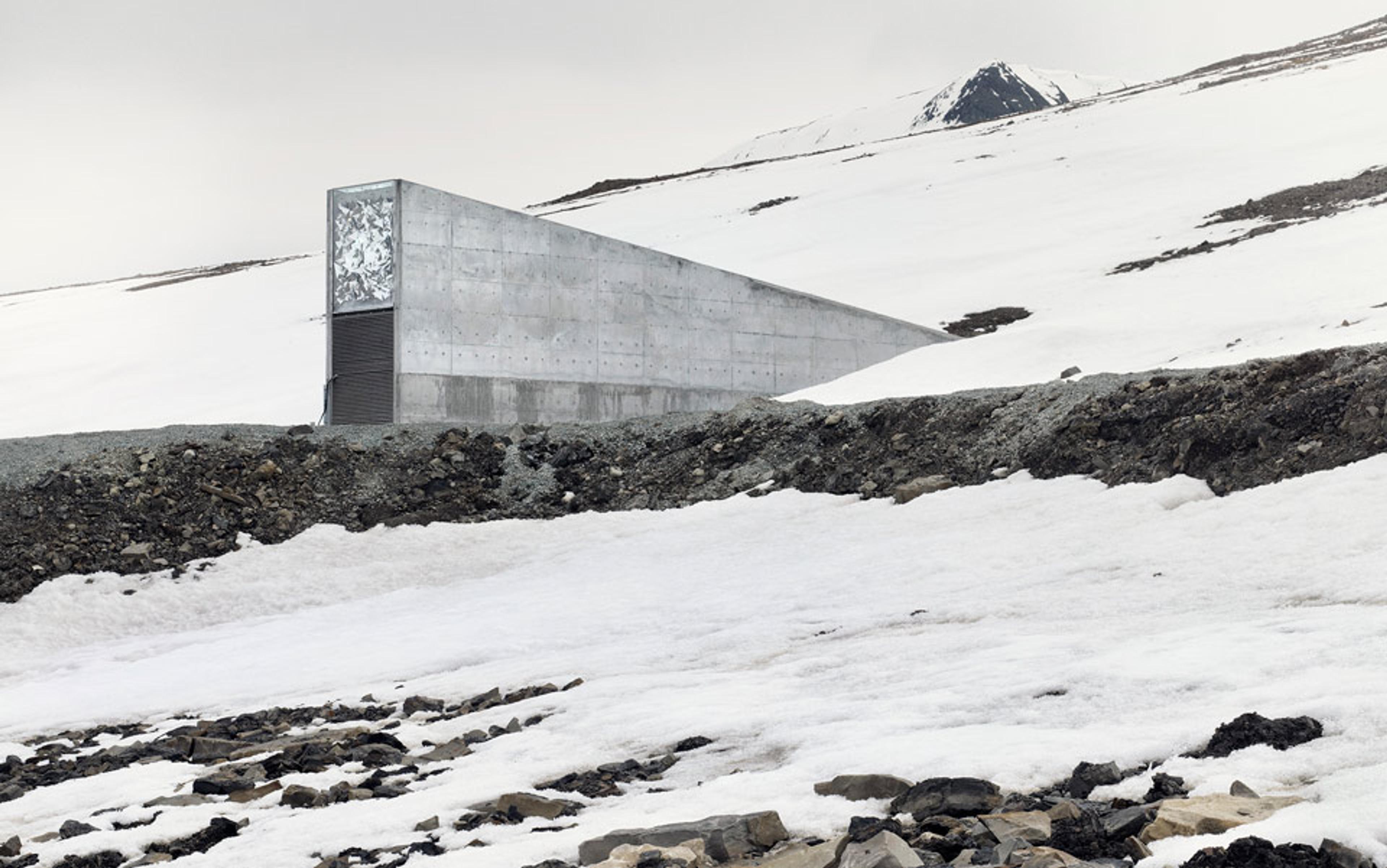 A concrete building partially covered in snow on a barren, snowy landscape with a mountain in the background.