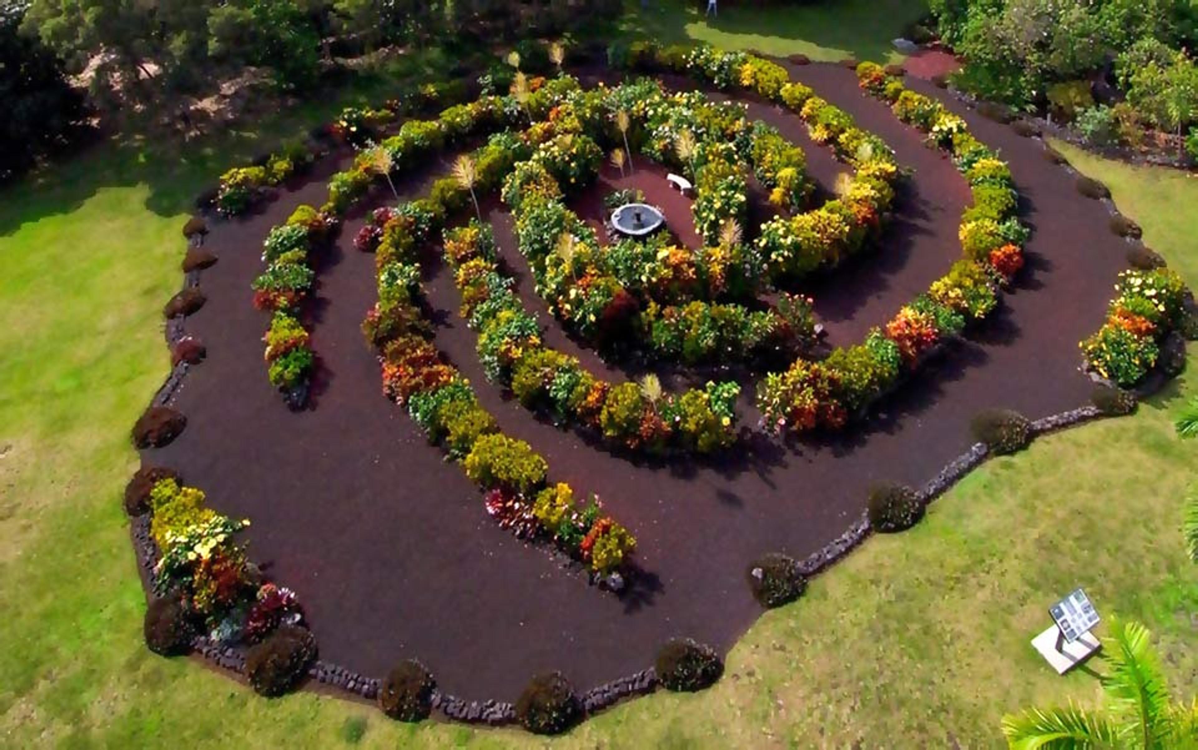 Photo of a garden with a plant spiral, central fountain, and well-maintained pathways, surrounded by lush greenery.