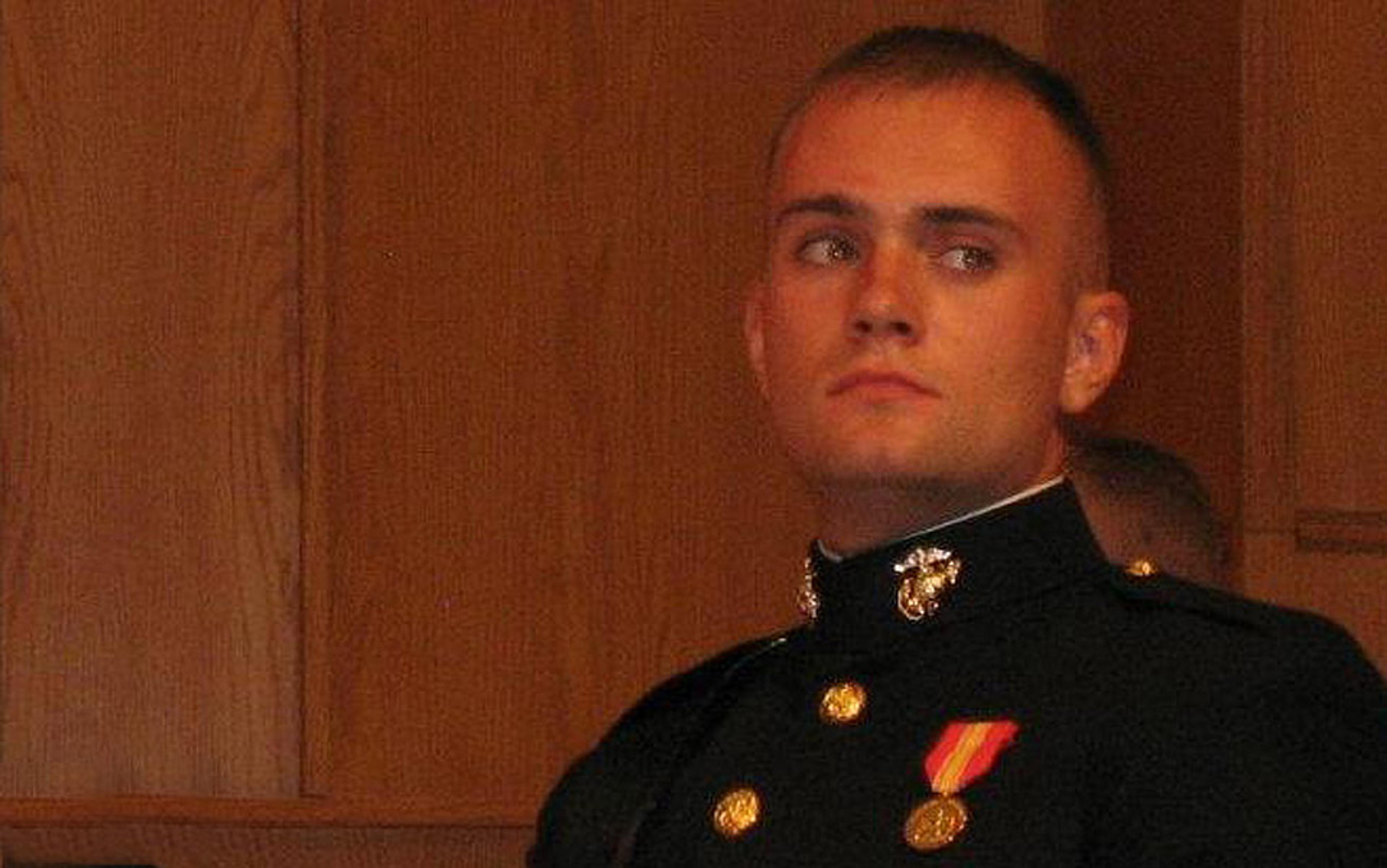 A man in a military dress uniform with medals, looking thoughtful, against a background of wooden panels.