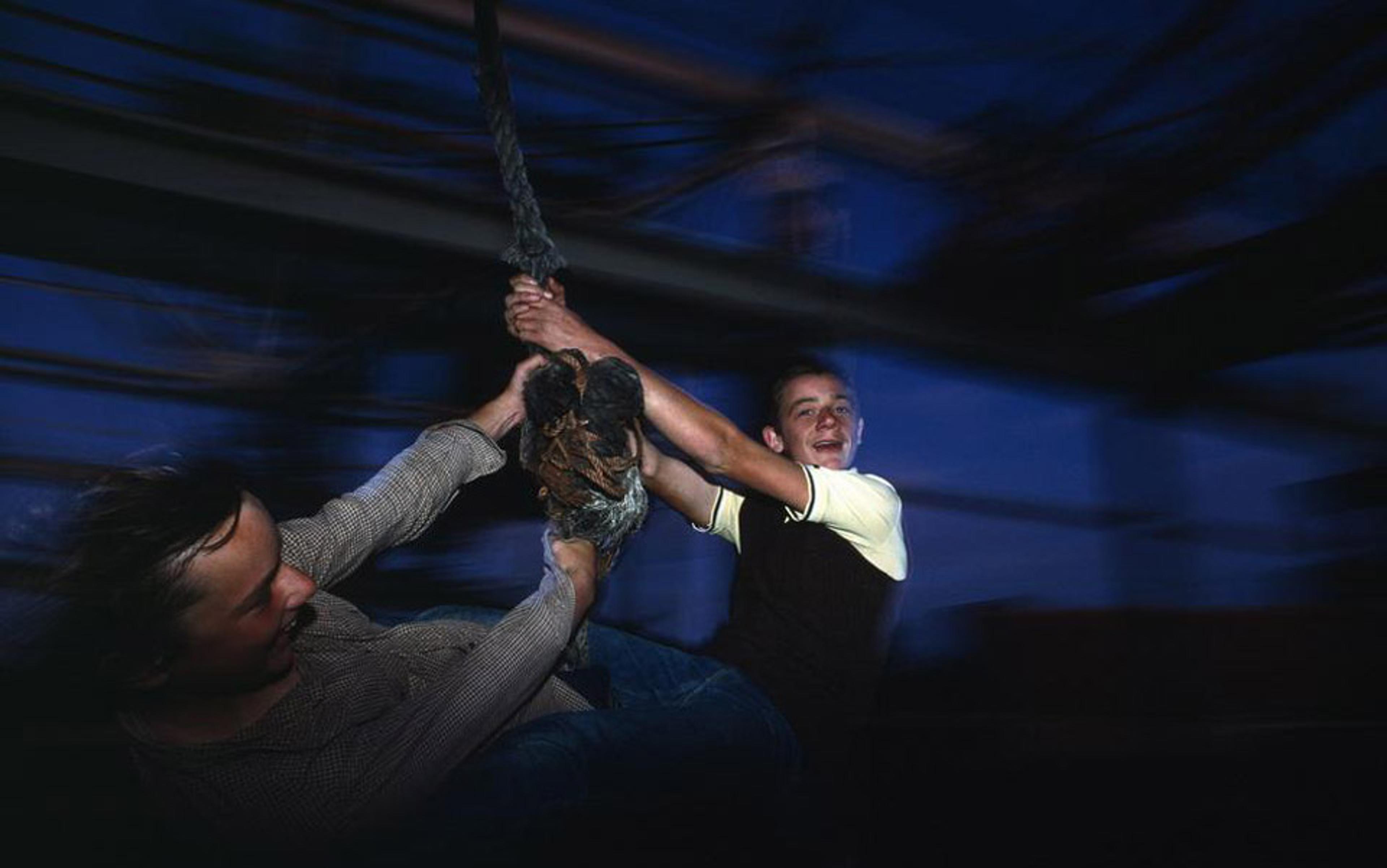 A photo of two people holding onto a rope swing with motion blur in a dark setting, expressing joy and excitement.