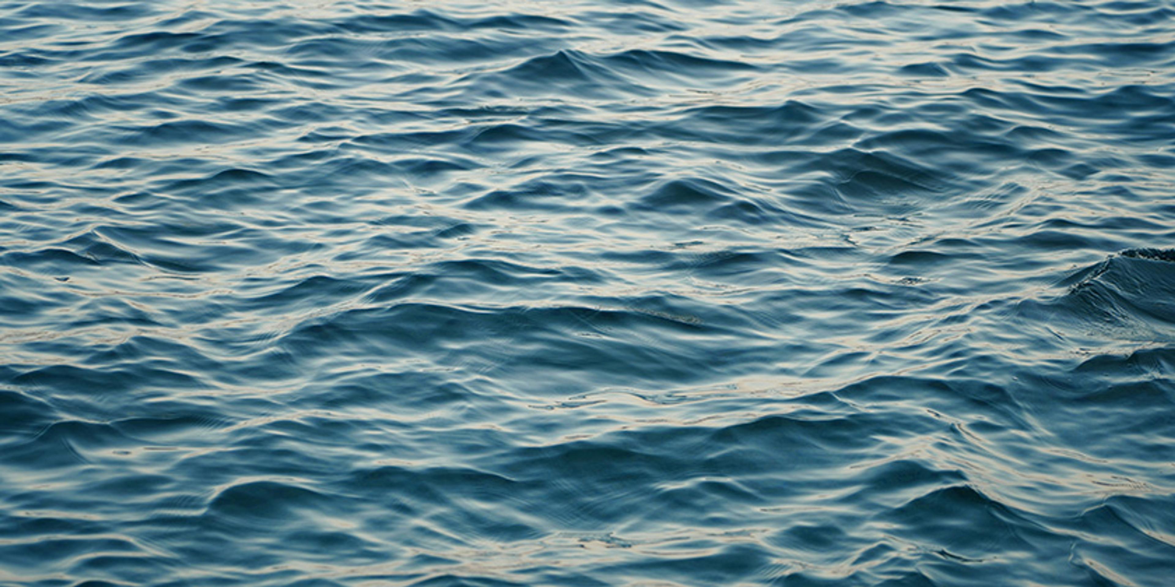 Photo of a calm sea with gentle waves and ripples on the water’s surface, reflecting a soft light.