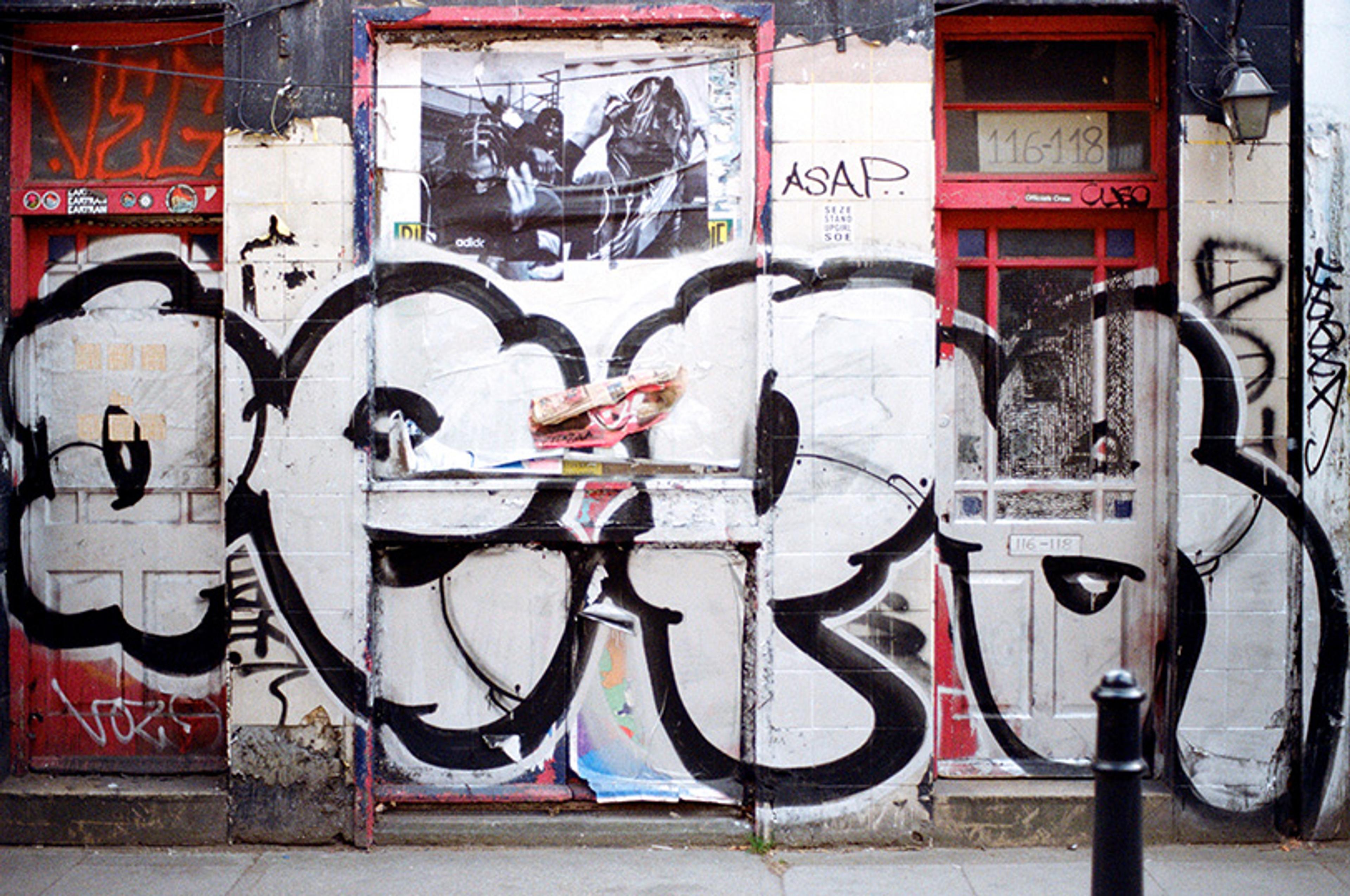 Photo of an urban wall with bold graffiti and posters across red doors, creating a gritty street art vibe.