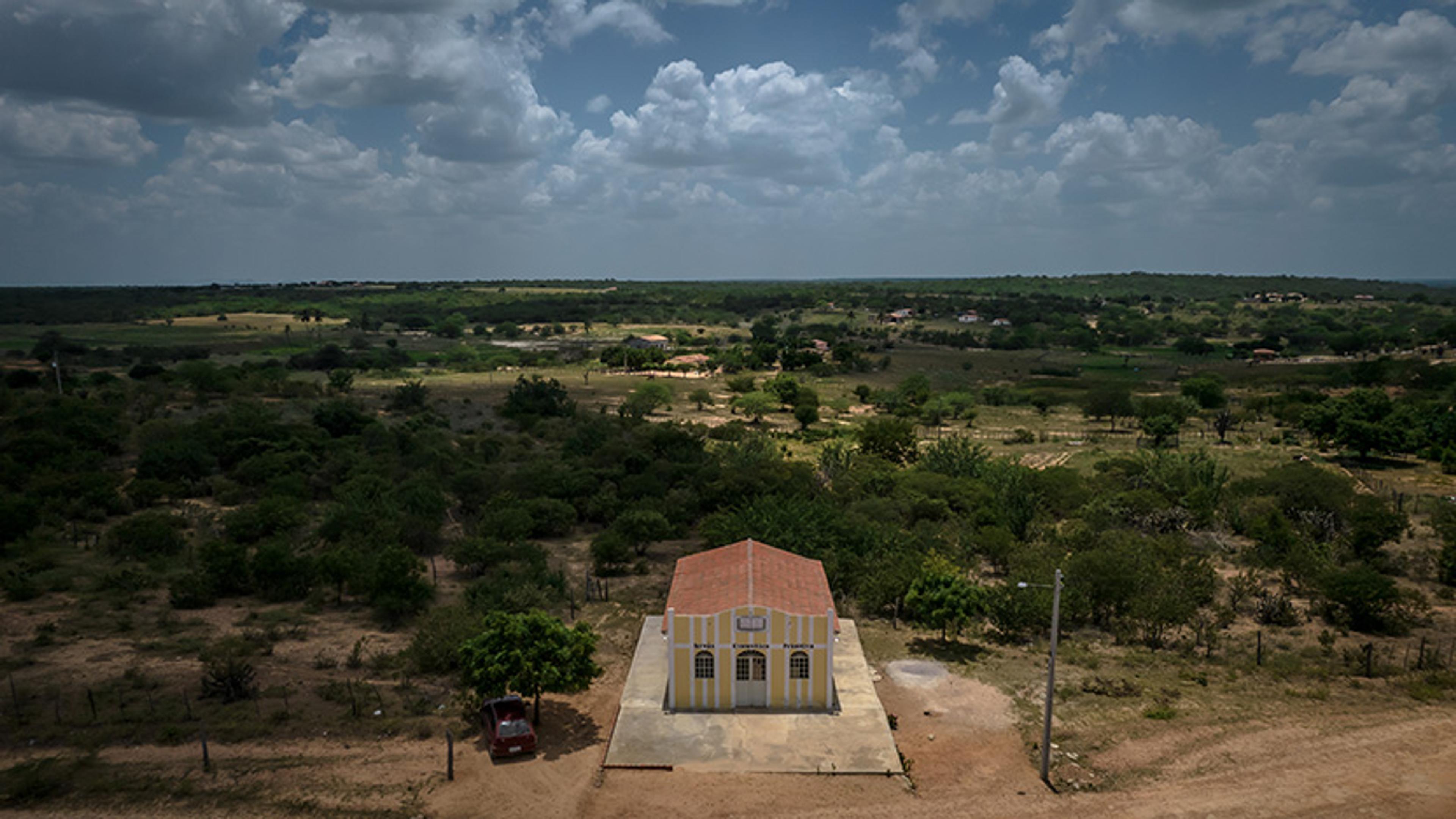 Aerial photo of a small building with a red roof in a rural landscape under a partly cloudy sky.