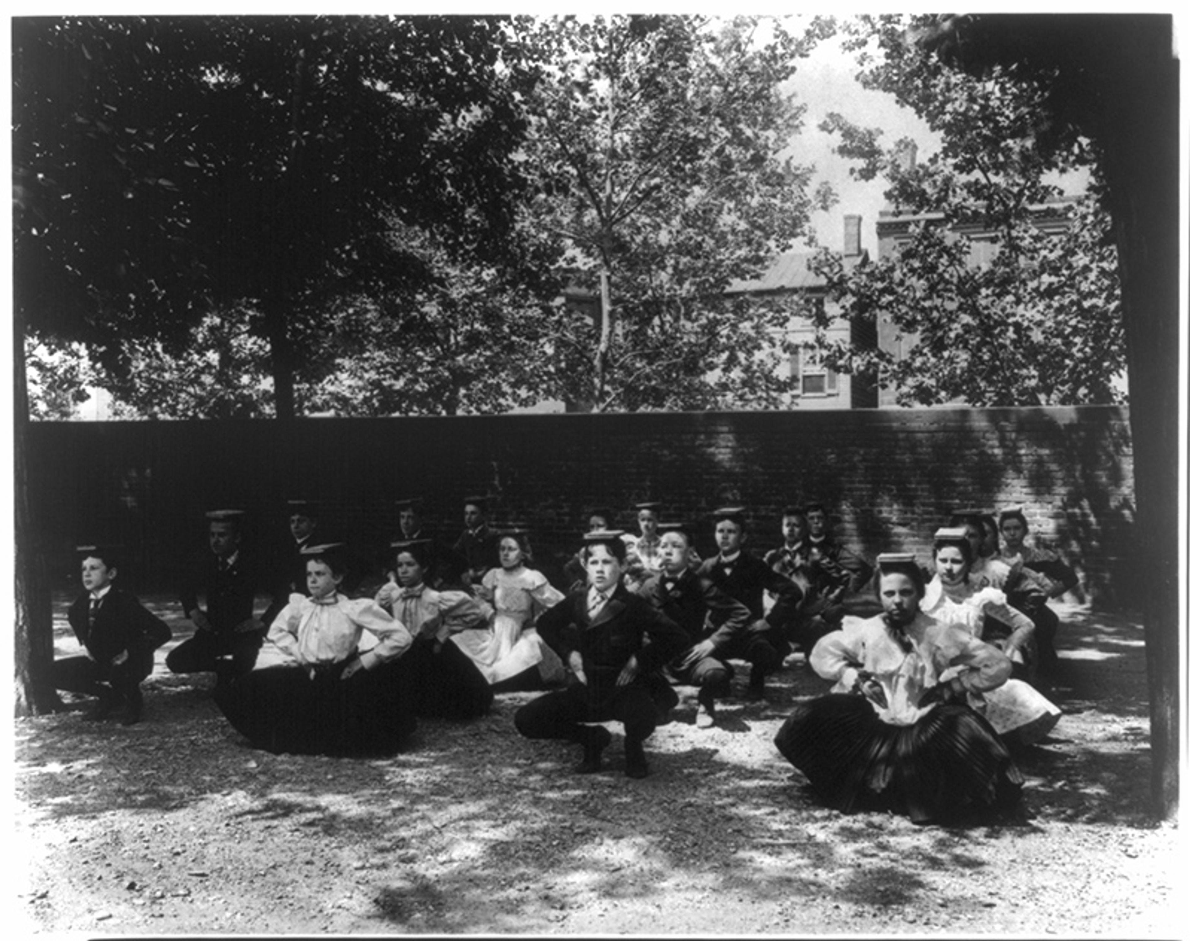 Black and white photo of young people in early 20th century clothing posing in an outdoor setting with trees in the background.