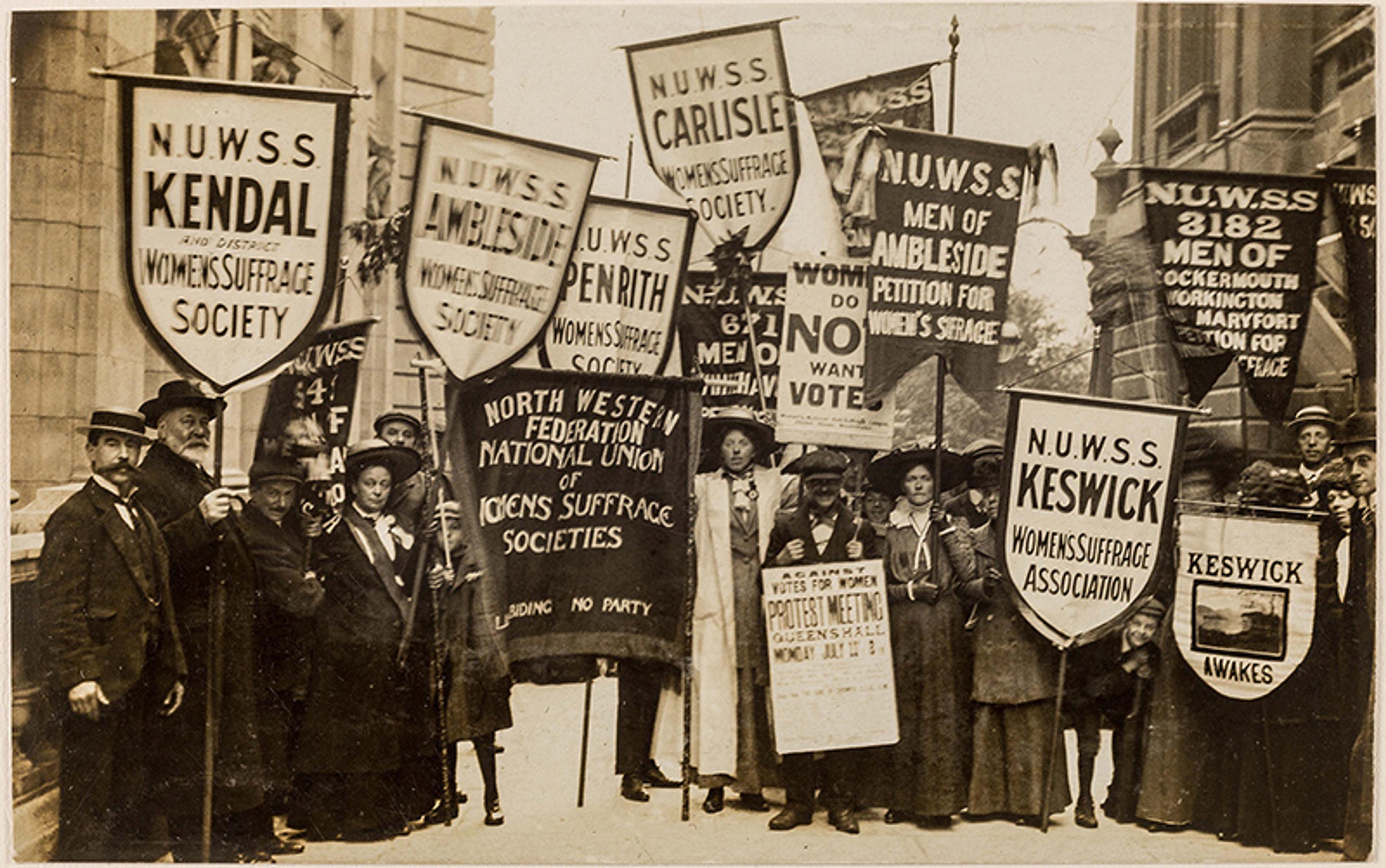 Black-and-white photo of a women’s suffrage rally with people holding banners for voting rights and women’s suffrage societies.