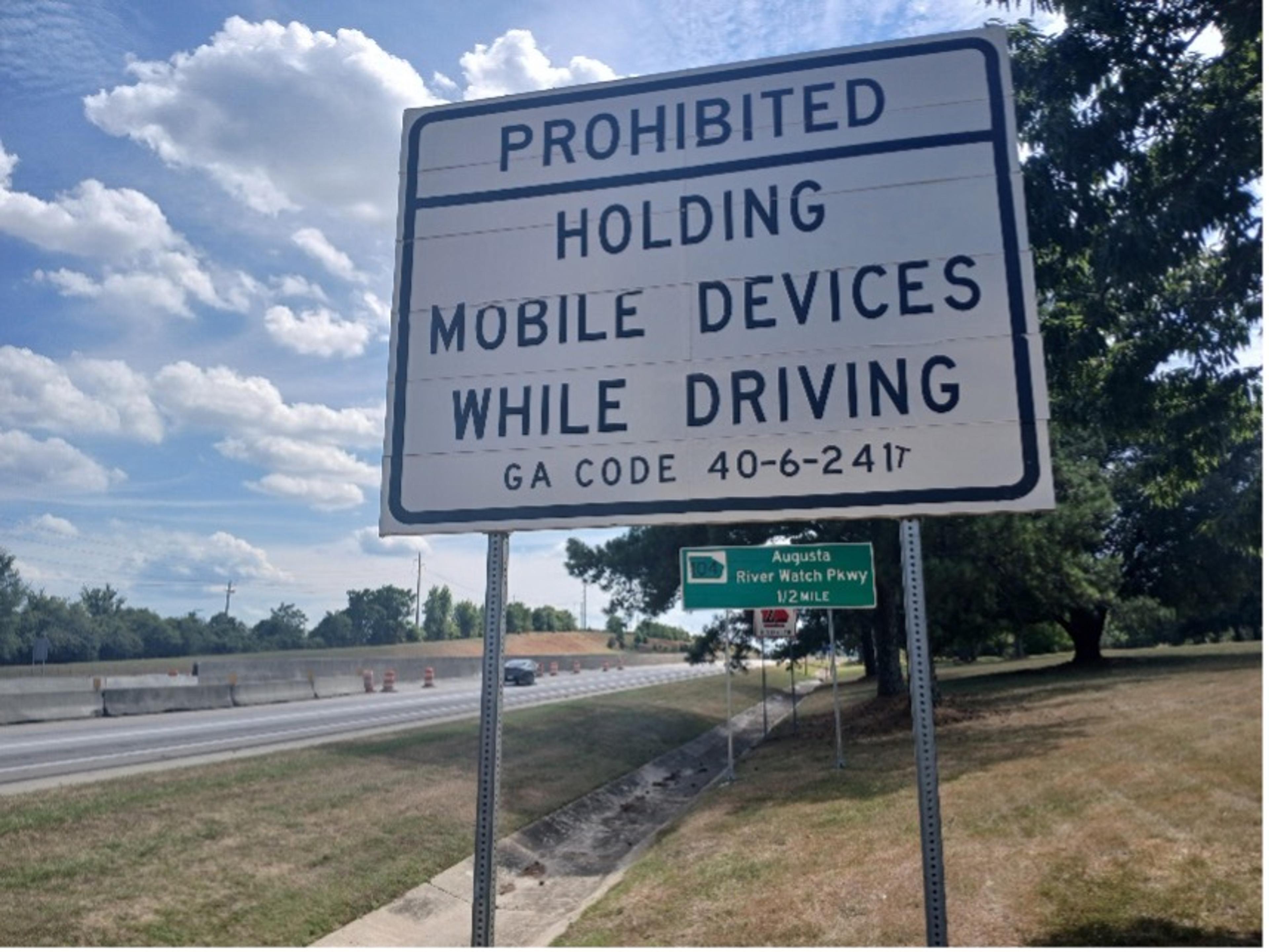 Photo of a road sign prohibiting holding mobile devices while driving in Georgia USA with a secondary road sign in the background.