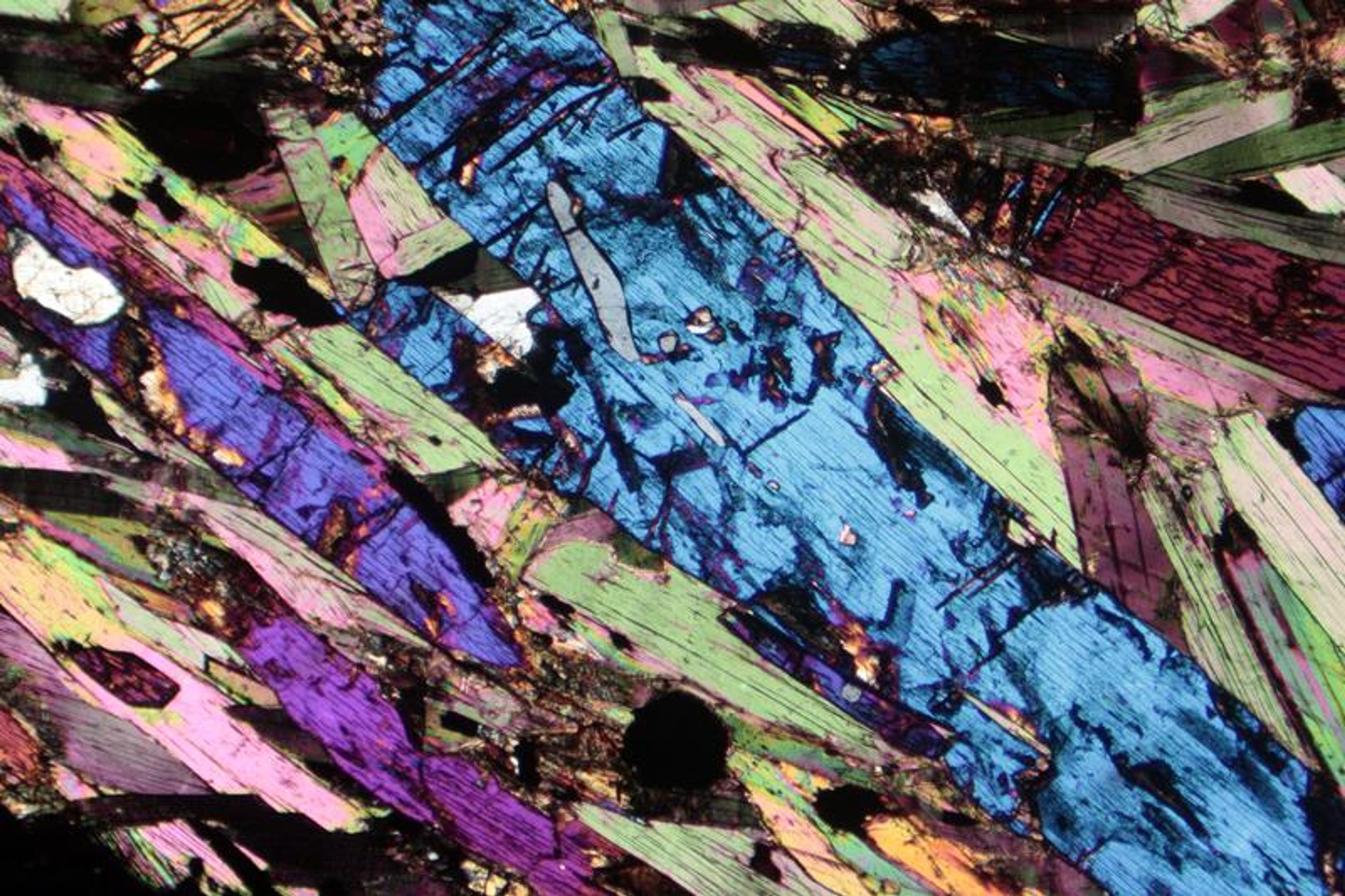 Photomicrograph of a rock slice showing vivid blue, pink and green mineral textures under polarised light.