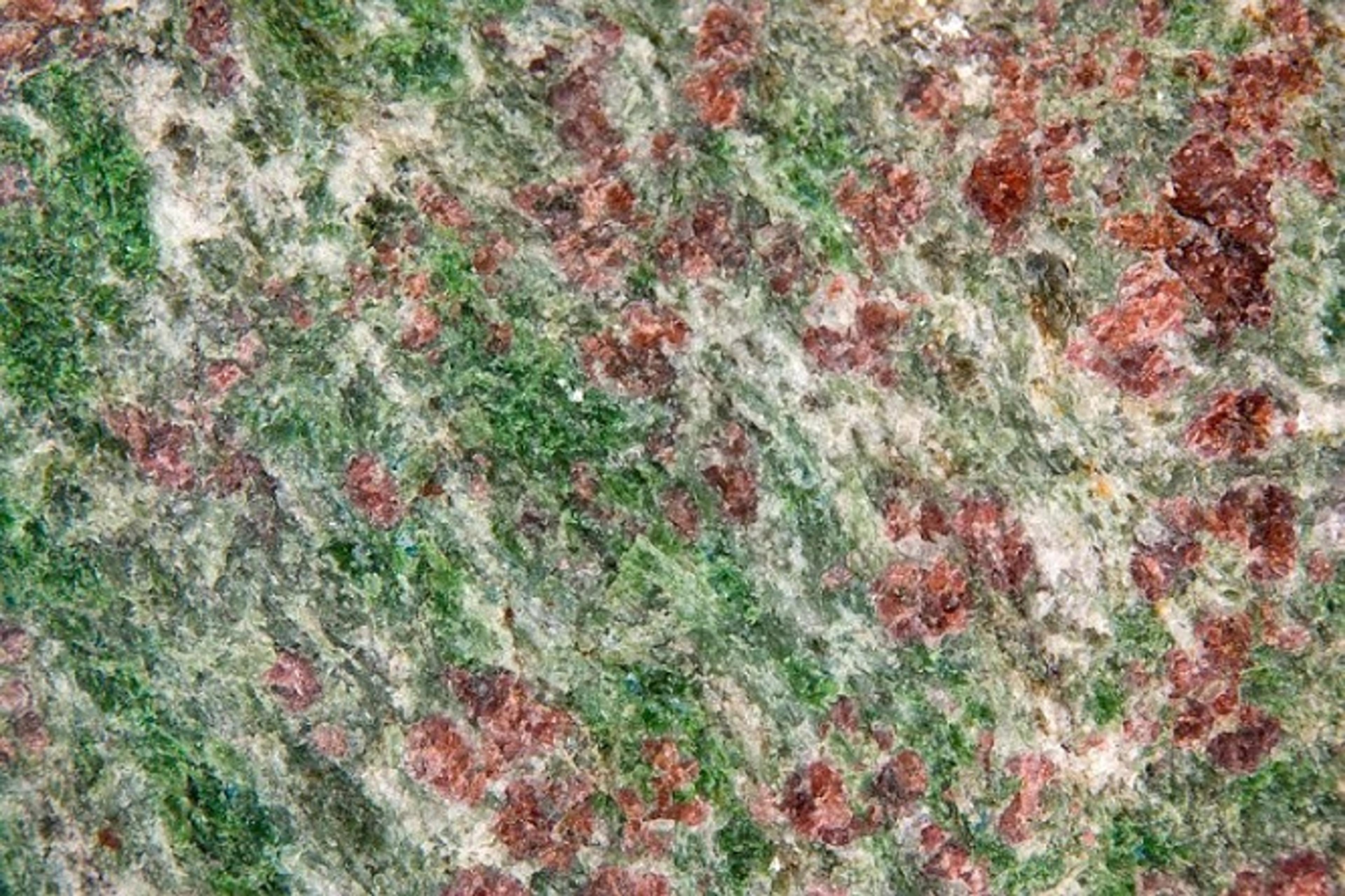 Close-up photo of a stone surface with green and red mineral patterns.