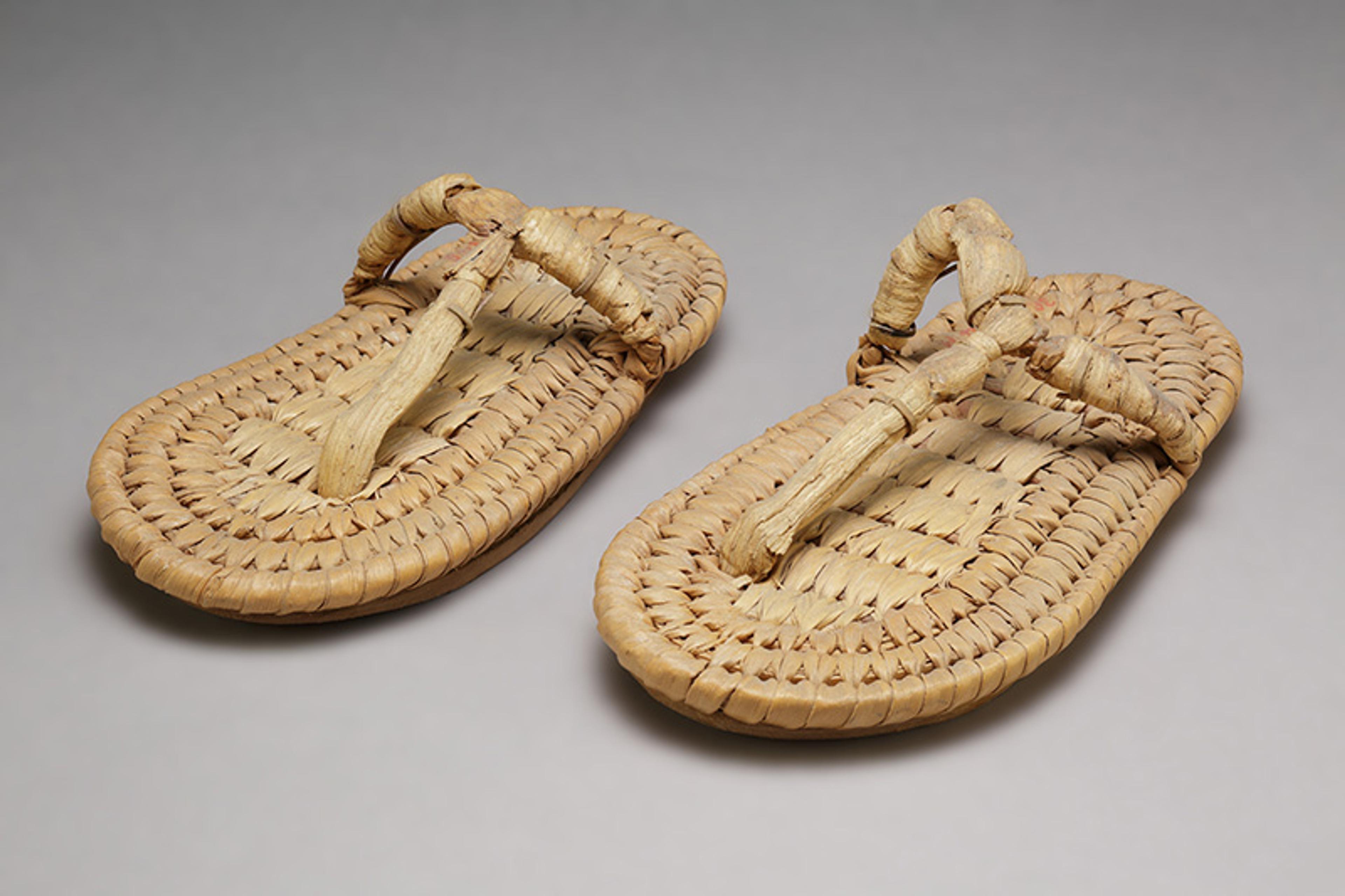 Photo of traditional woven straw sandals on a plain grey background.