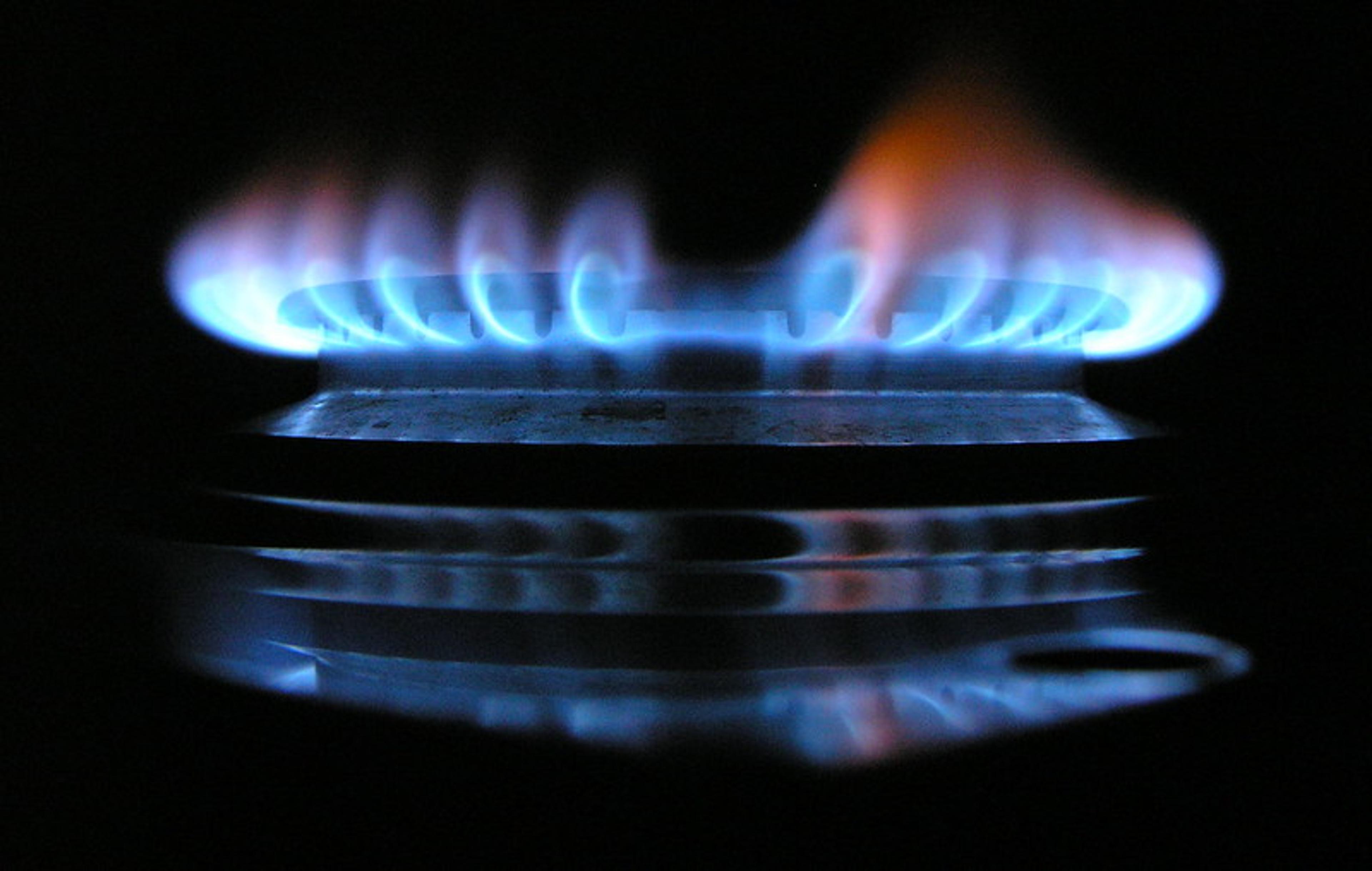 Close up of a lit gas stove burner emitting blue and orange flames in a dark setting.